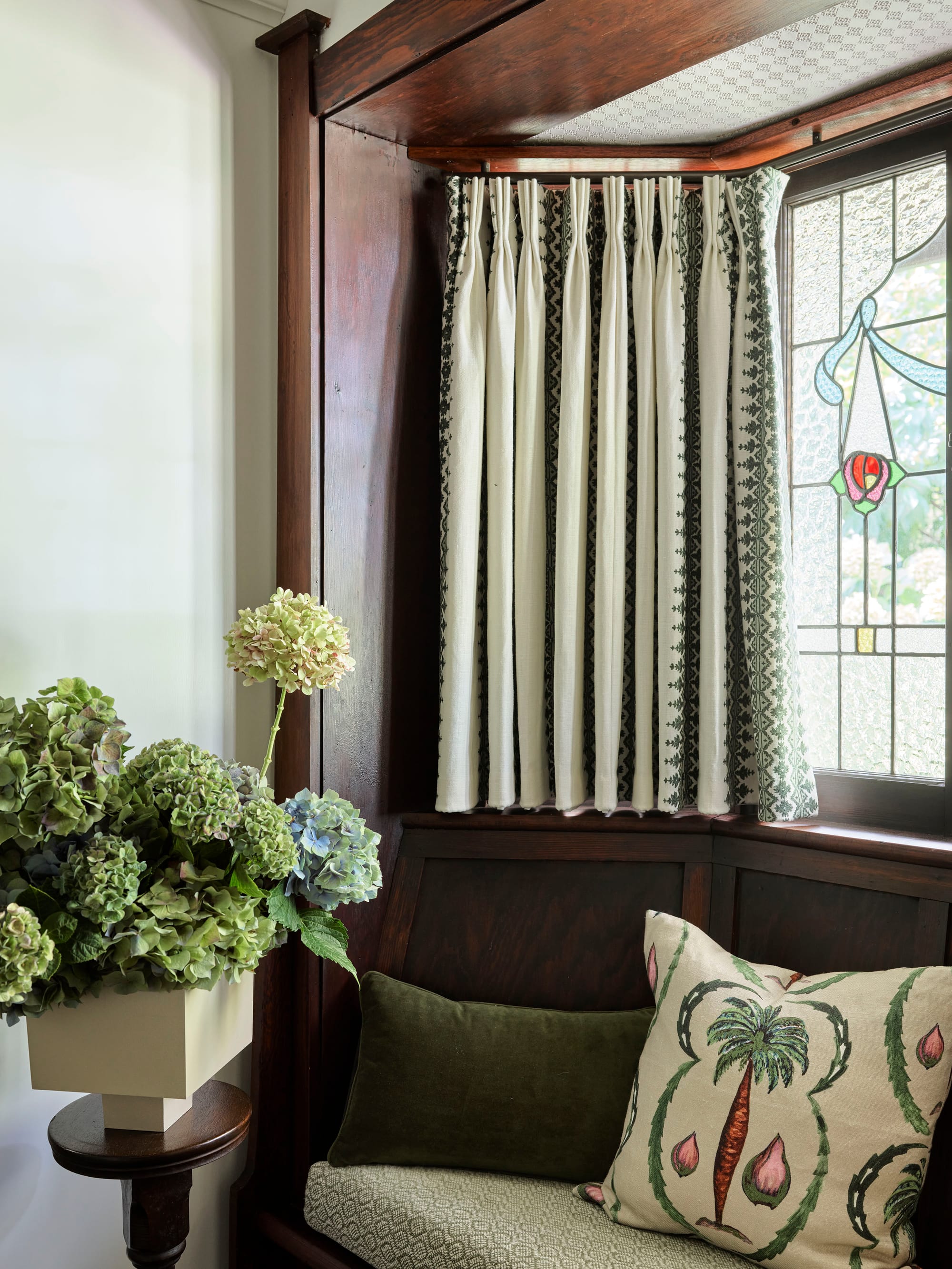 Ferris Street by Marylou Sobel Interior Design. Photography by Anson Smart. Dark timber bench seat with leadlight window above, green soft furnishings and floral arrangements. 