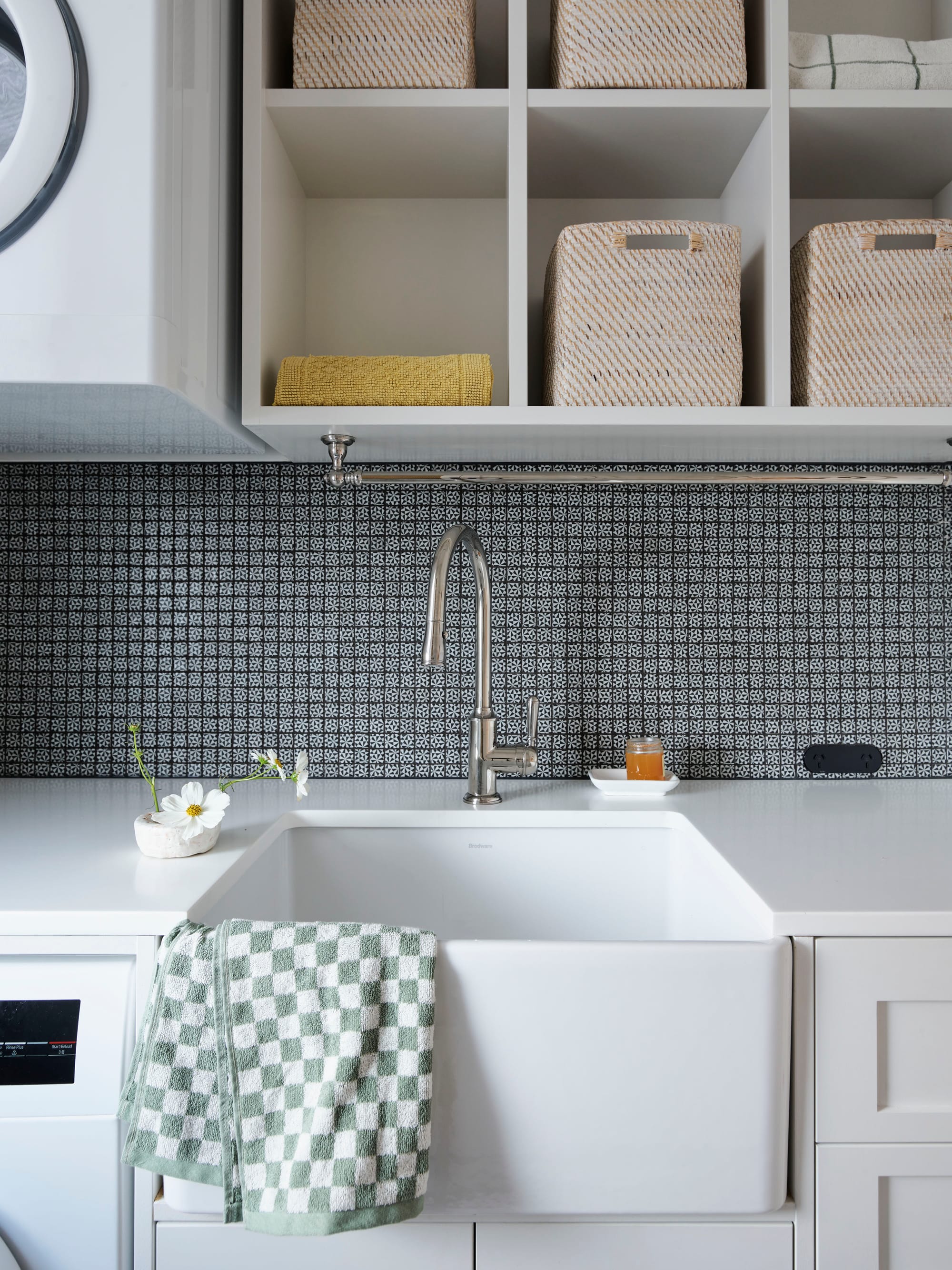 Ferris Street by Marylou Sobel Interior Design. Photography by Anson Smart. Laundry trough with checkered green and white hand towel, mosaic splashback and white overhead storage. 