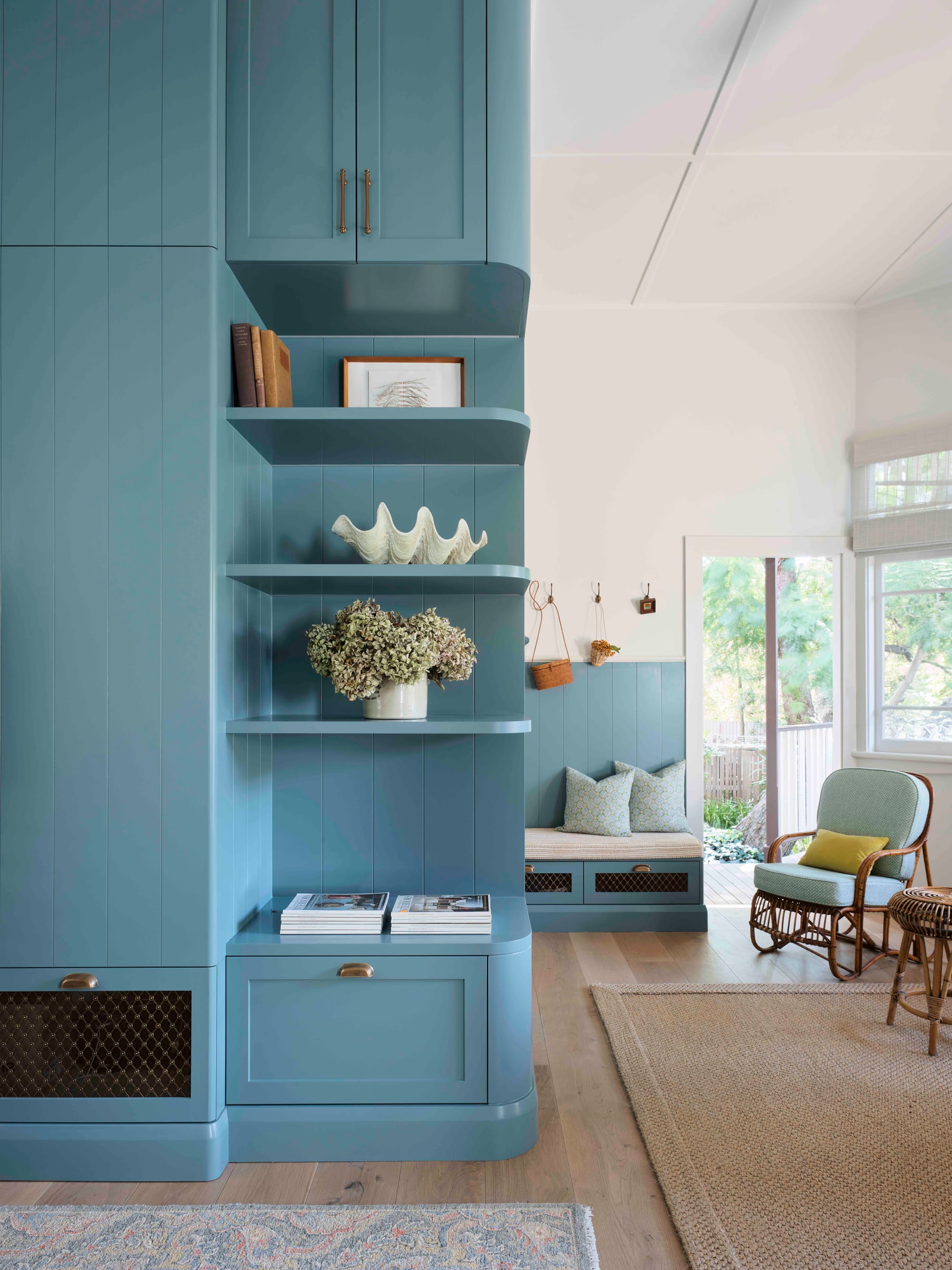 Ferris Street by Marylou Sobel Interior Design. Photography by Anson Smart. Full height blue integrated wall unit with open faced storage, timber flooring, patterned and jute rugs and with a small sitting area in background.
