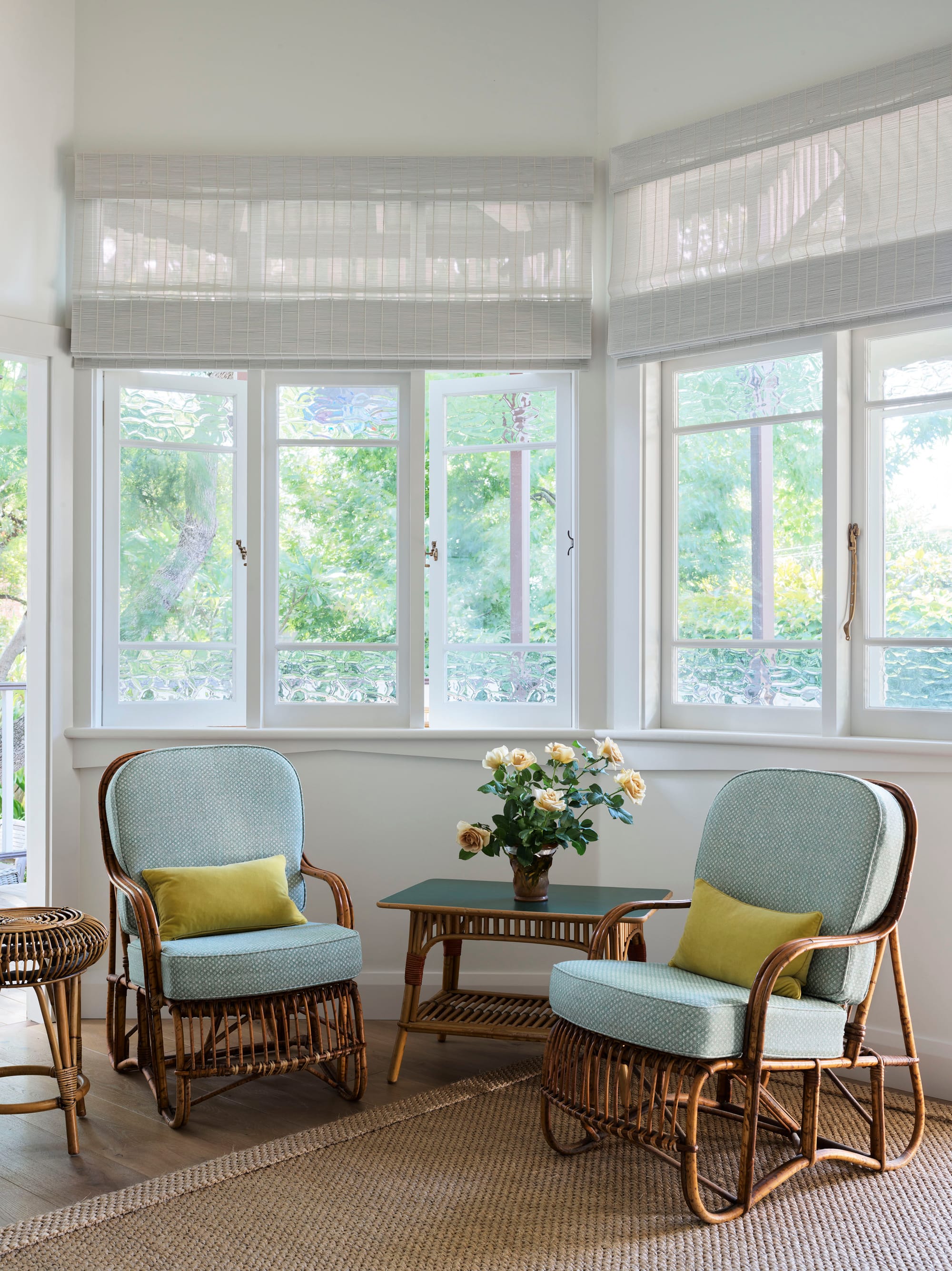 Ferris Street by Marylou Sobel Interior Design. Photography by Anson Smart. Sitting room with rattan armchairs and side tables with teal cushions, positioned on timber floor and jute rug and underneath curved windows. 