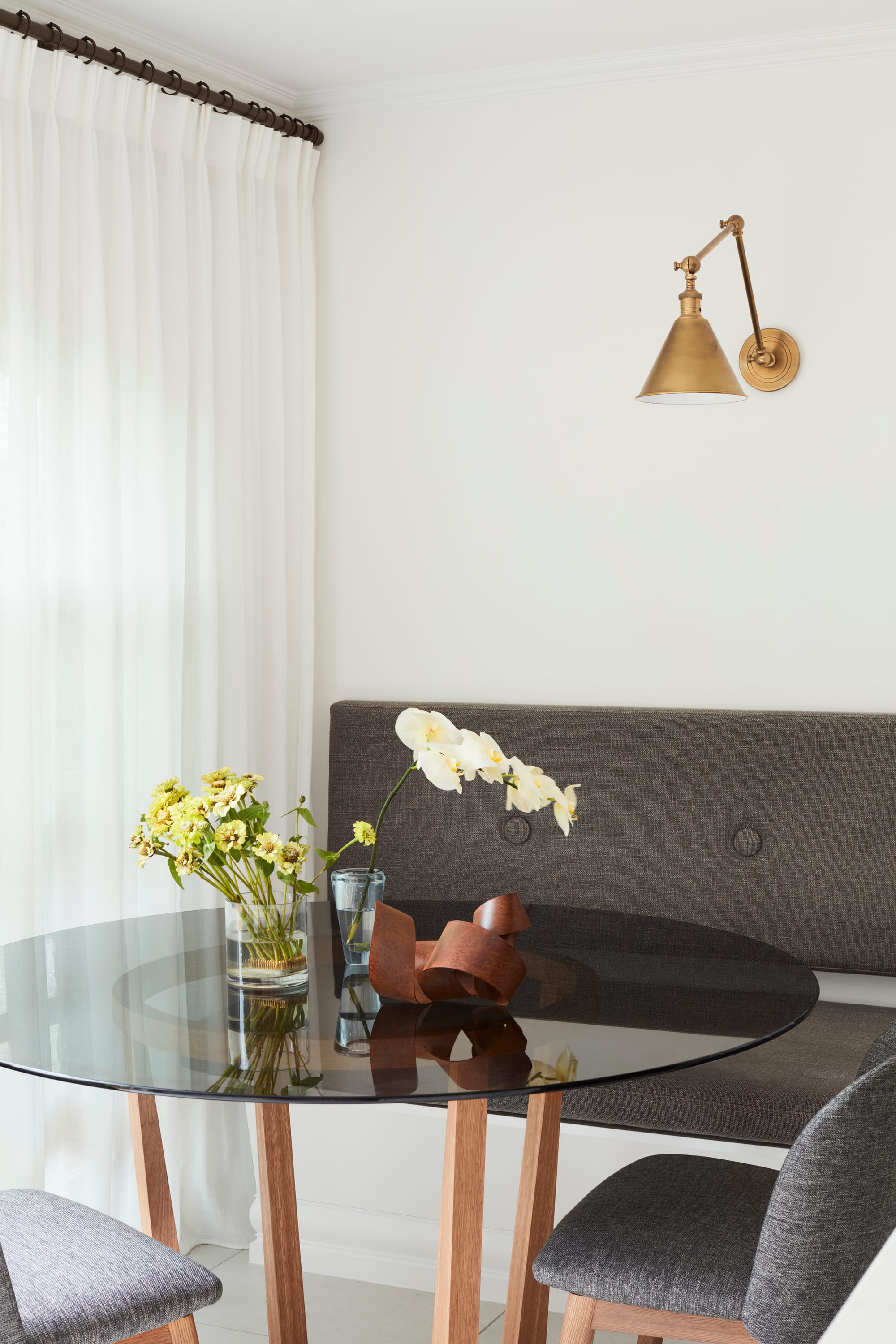 Marathon Road by Marylou Sobel Interior Design. Photography by Prue Ruscoe. Breakfast nook with integrated bench seating with grey fabric finish, matching dining chairs and round dining table with smoked glass tabletop. 