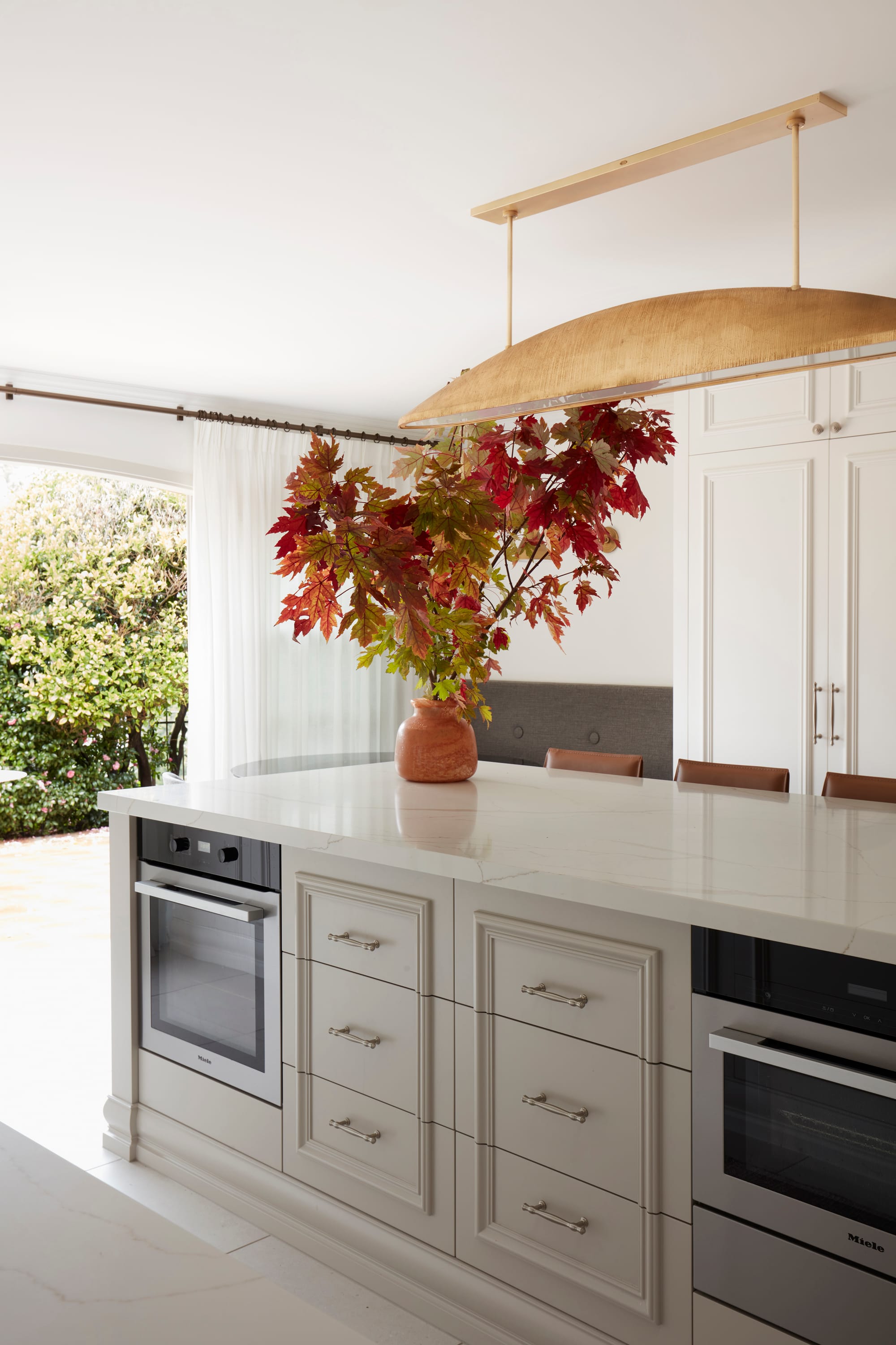 Marathon Road by Marylou Sobel Interior Design. Photography by Prue Ruscoe. Kitchen with beige cabinetry on island bench, white stone benchtop and large door connecting to the garden. 