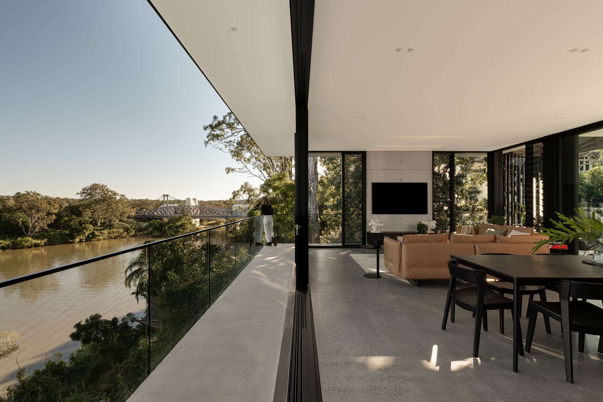The River House, Indooroopilly by Sarah Waller Architecture. Photography by Alyne Media. Woman stands at the corner of a balcony.