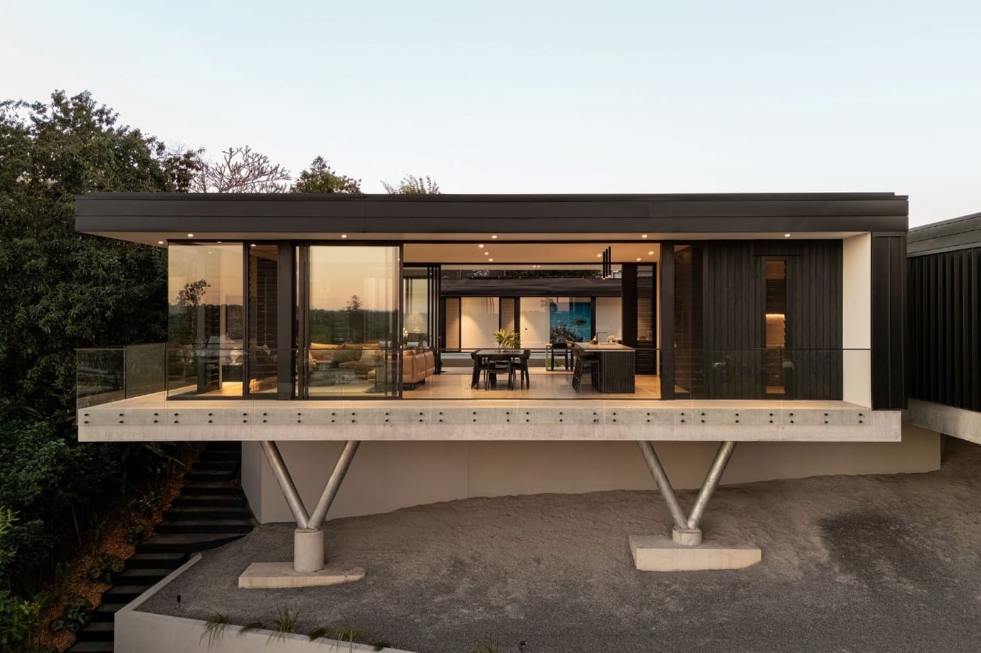 The River House, Indooroopilly by Sarah Waller Architecture. Photography by Alyne Media. House suspended over a cliffside with long balcony, glass balustrade and black, flat roof. 