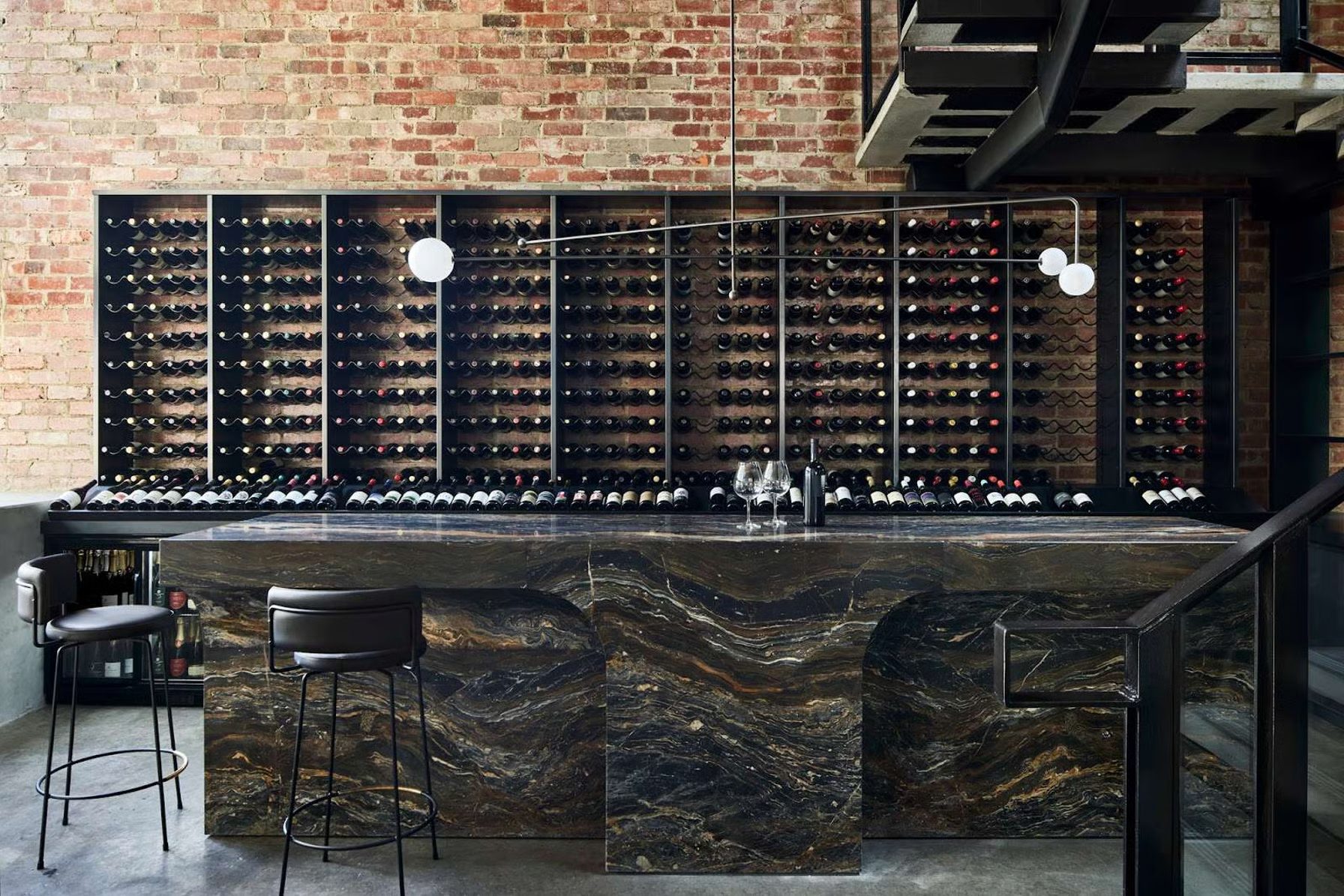 Saint Hotel by Telha Clarke Architecture & Design. Photography by Sharyn Cairns. A striking wine bar features a dramatic stone counter paired with a full-height wine rack against an exposed brick wall.