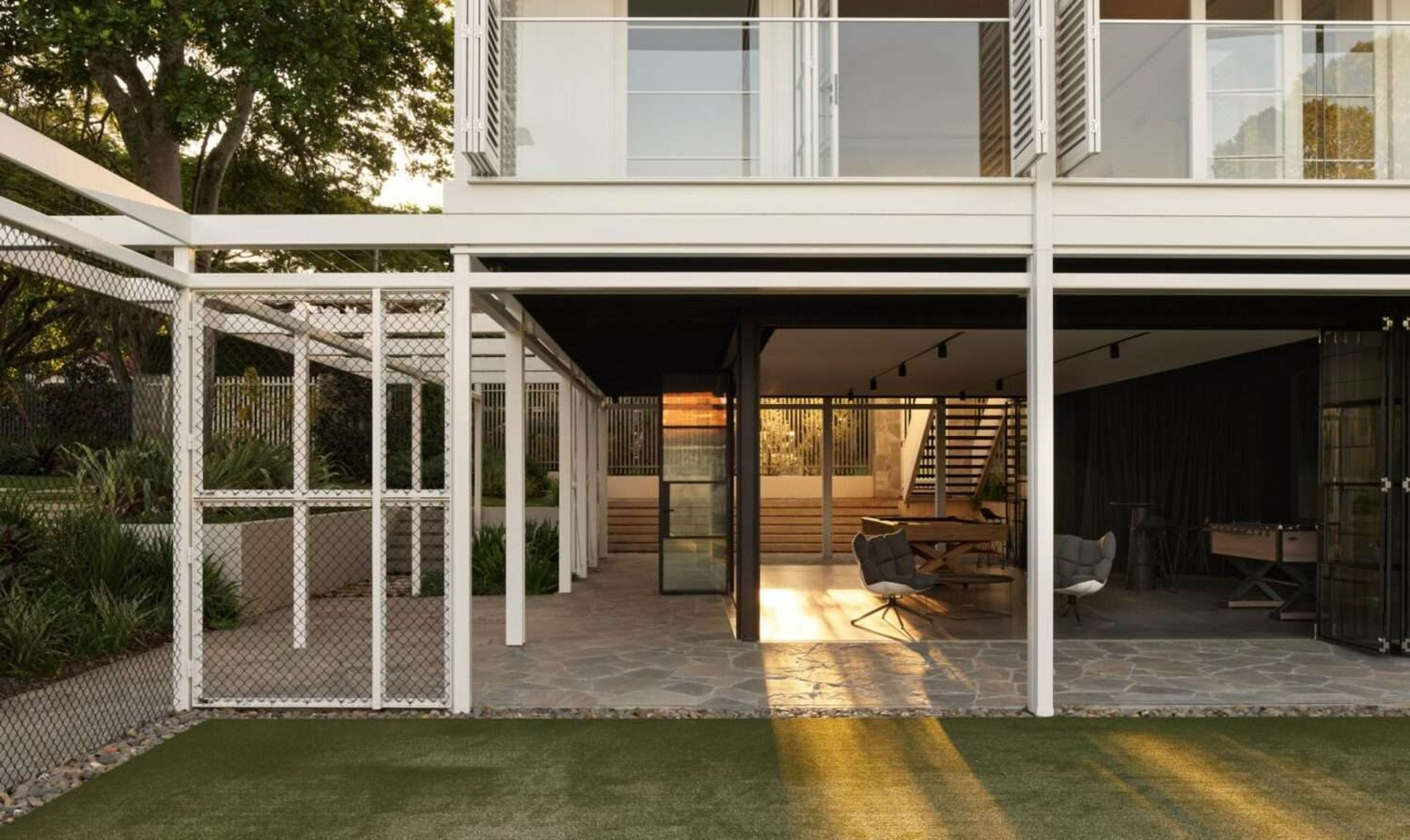 Ascot Club House by Alexandra Buchanan Architecture. Architecture by Toby Scott. Golden light shining through the bottom, open air floor of a double storey, white clad Queenslander. 