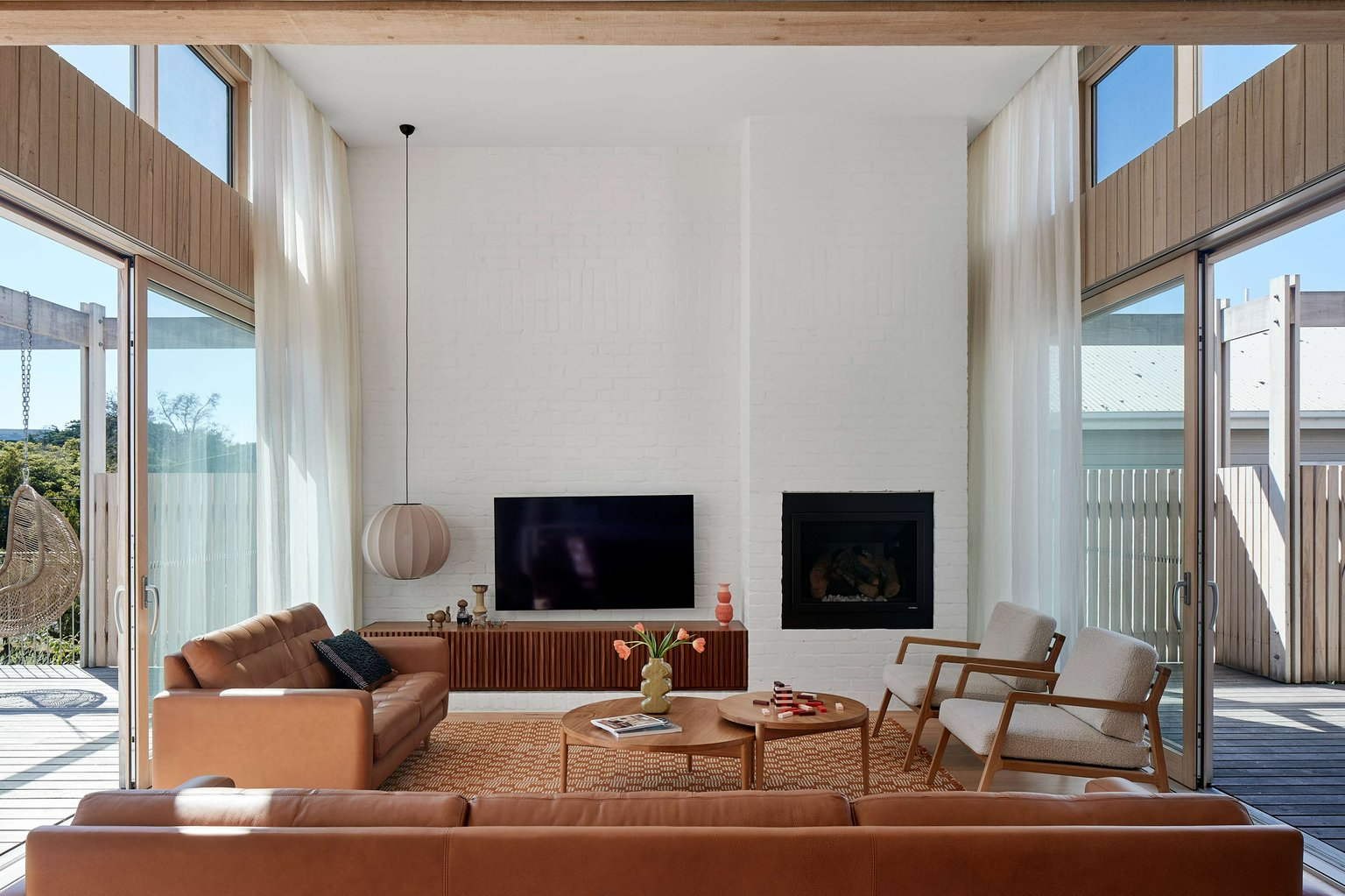 The Blairgowrie Beach Club by Bower Architecture & Interiors. Photography by Shannon McGrath. Living space with high ceilings, white brick walls, integrated fireplace and warm toned furnishings. 