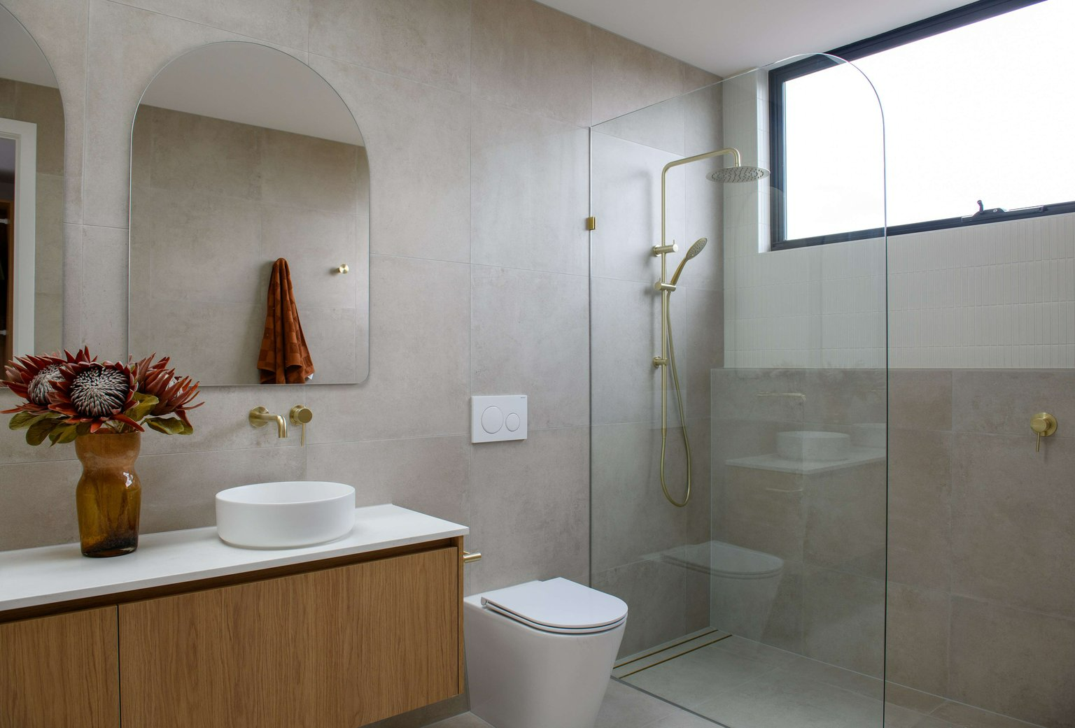 East Keilor One by Eastwood Designers. Photography by Tanya Macheda. Bathroom with beige wall and floor tiles, a timber vanity and a glass shower screen.  