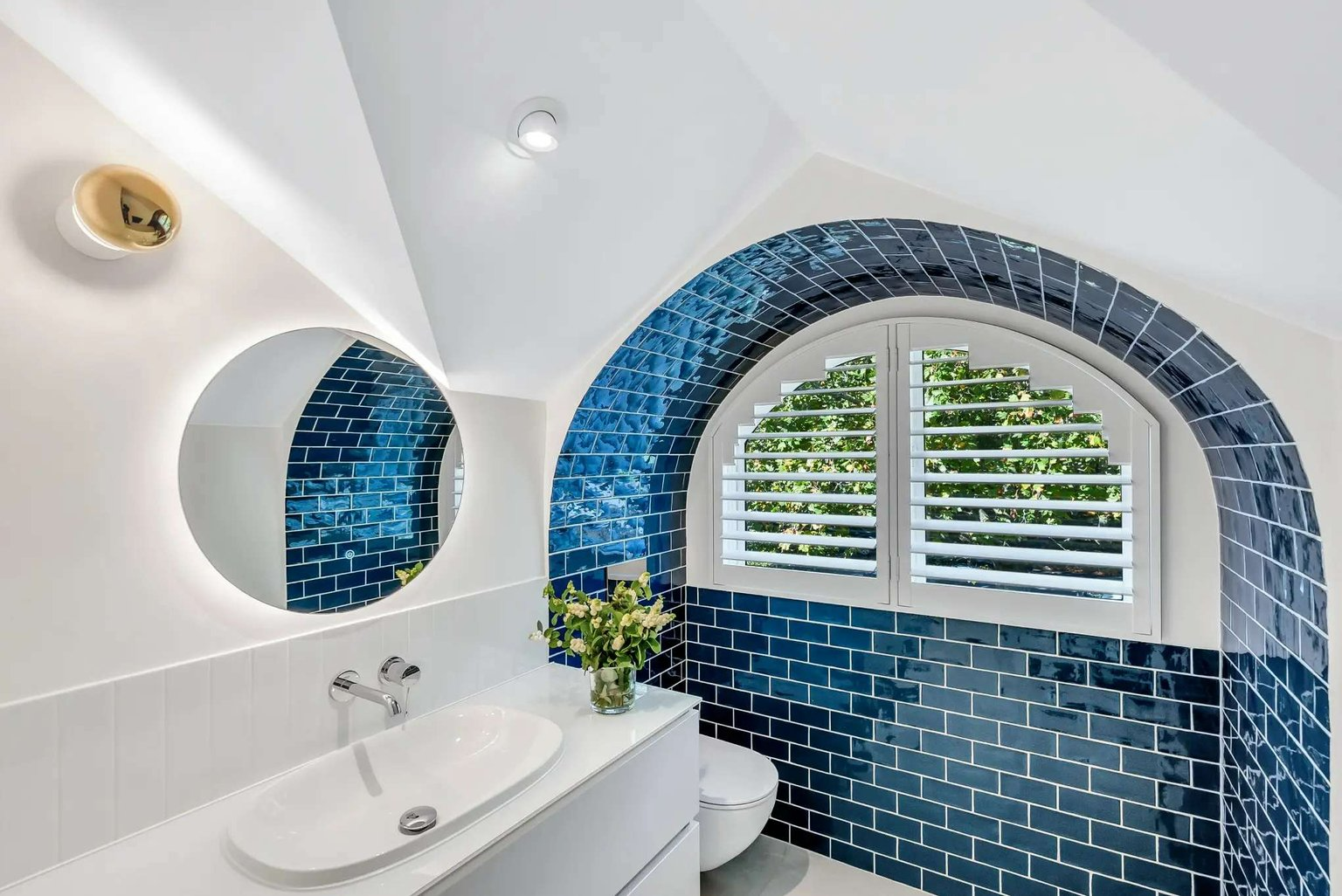 Cozy Retreat by Emotive Designs. Bathroom with white walls and counter with a curved window, tiled in blue subway tiles.