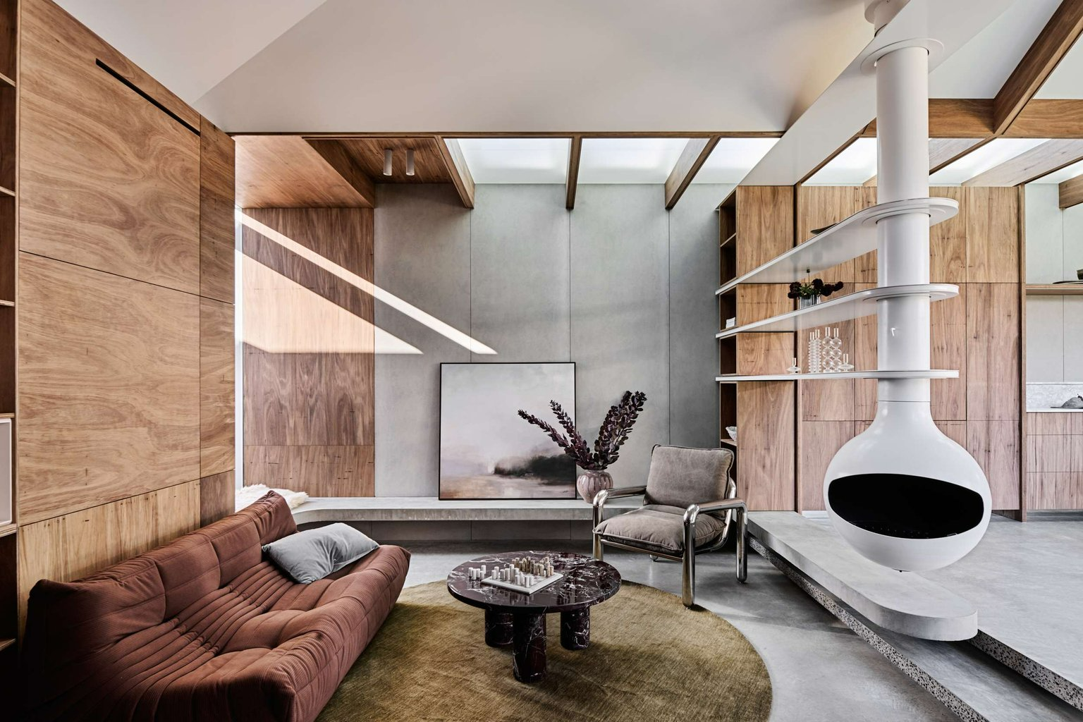 Hug House by FIGR Architecture Studio. Photography by Tom Blachford. MCM inspired sunken living space with suspended, circular white fireplace, terracotta couch and timber paneled walls. 