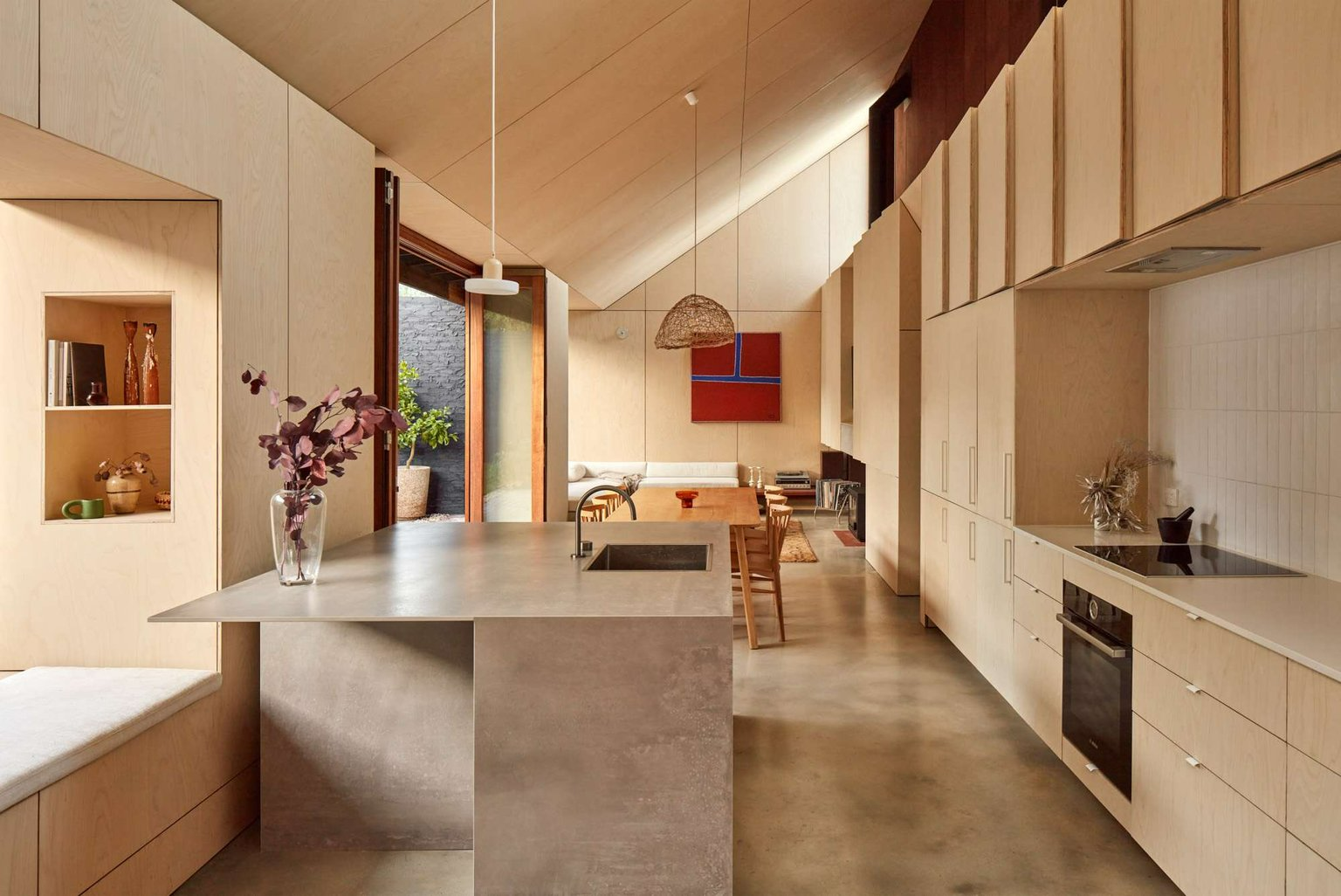 Shadow House by Grotto Studio. Photography by Jack Lovel. Open plan home with pitched, plywood clad ceilings, an asymmetrical concrete and steel island bench and integrate cabinetry throughout. 