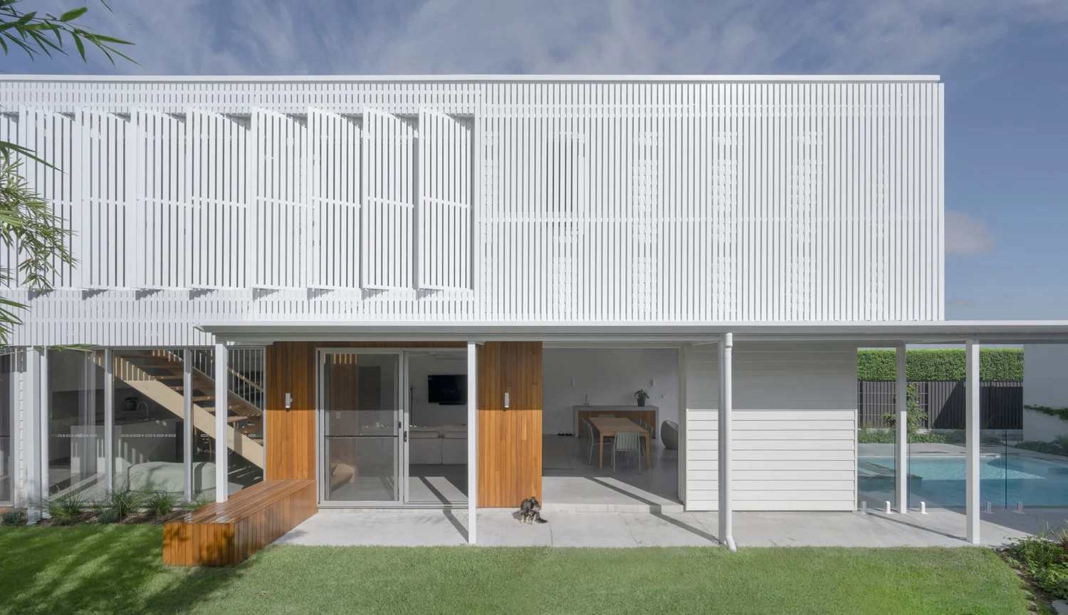 Veil + CO.House by Kirsten Johnstone Architects. Photography by Alanna Jayne McTiernan. Exter facade of pavilion home with white shutters, patio, timber detailing and green grass. 