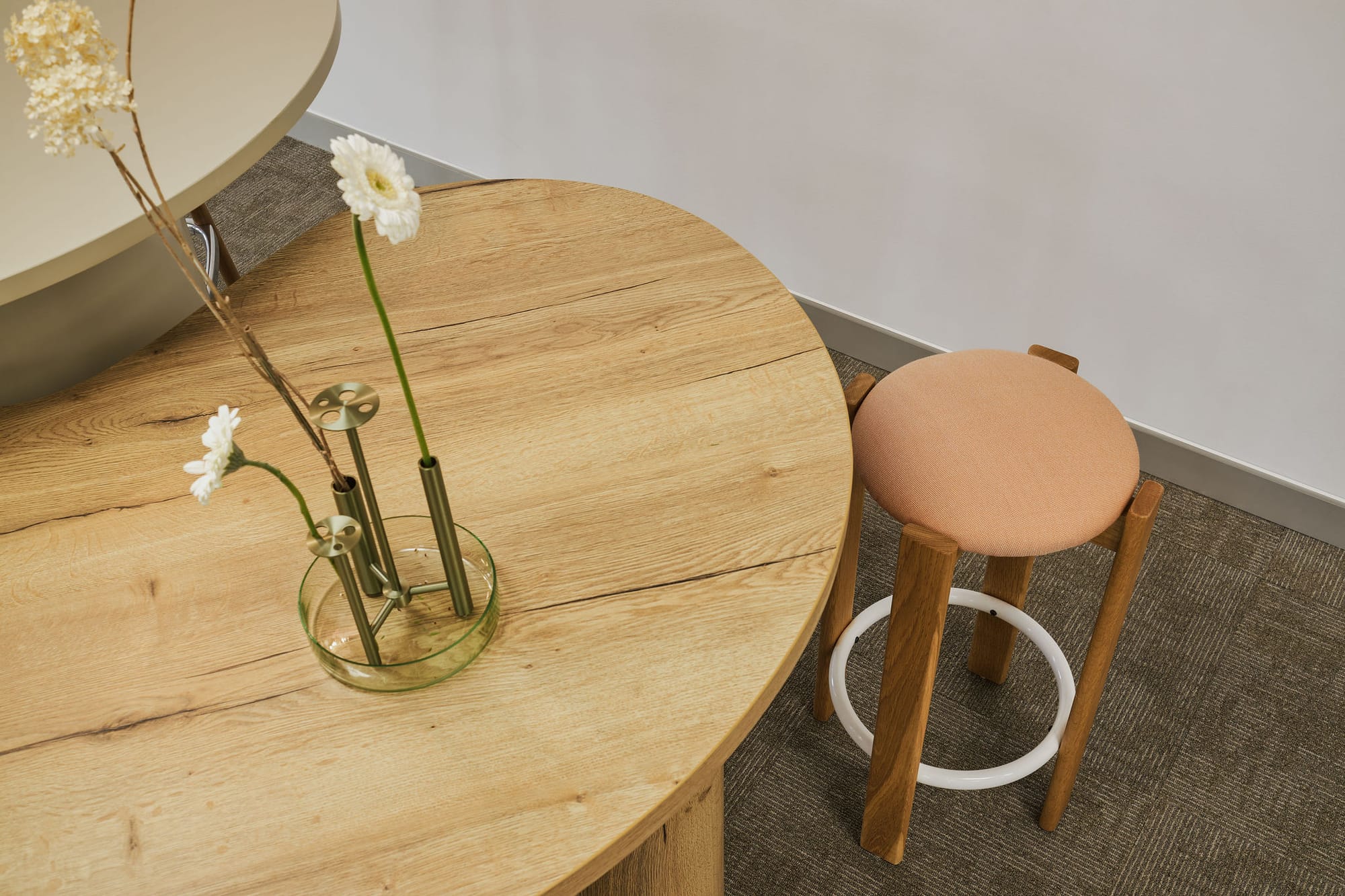 Project Kubo by M&E Interiors. Round timber table with timber stool with pink seat cushion, in room with grey carpet. 