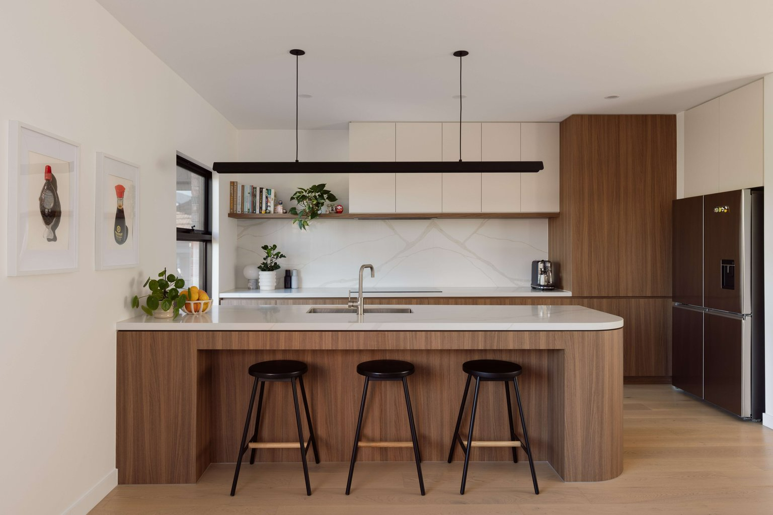Maud by Mancini Made. Photography by Elise Scott. Mid century modern inspired kitchen with timber cabinetry and island, white splashback and benchtops and black stools. 