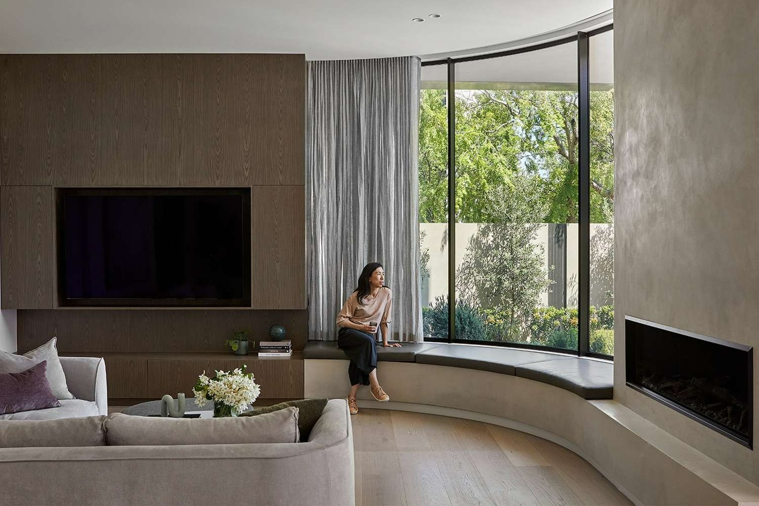 The Bronze House by Merrylees Architecture & Interior Design. Photography by Dave Kulesza. Living space with curved feature window, fireplace on limewashed wall, leather window seatand timber floors.