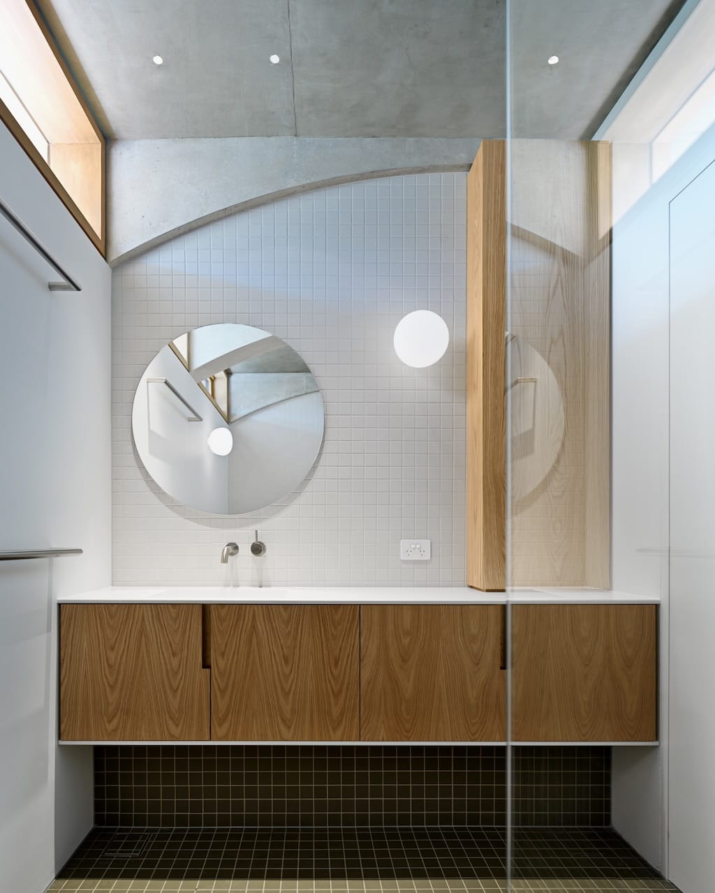 Corbel House by Nick Bell Architects. Photography by Justin Alexander. Bathroom with olive floor tiles, white tiled walls, timber cabinet and circle mirror. 