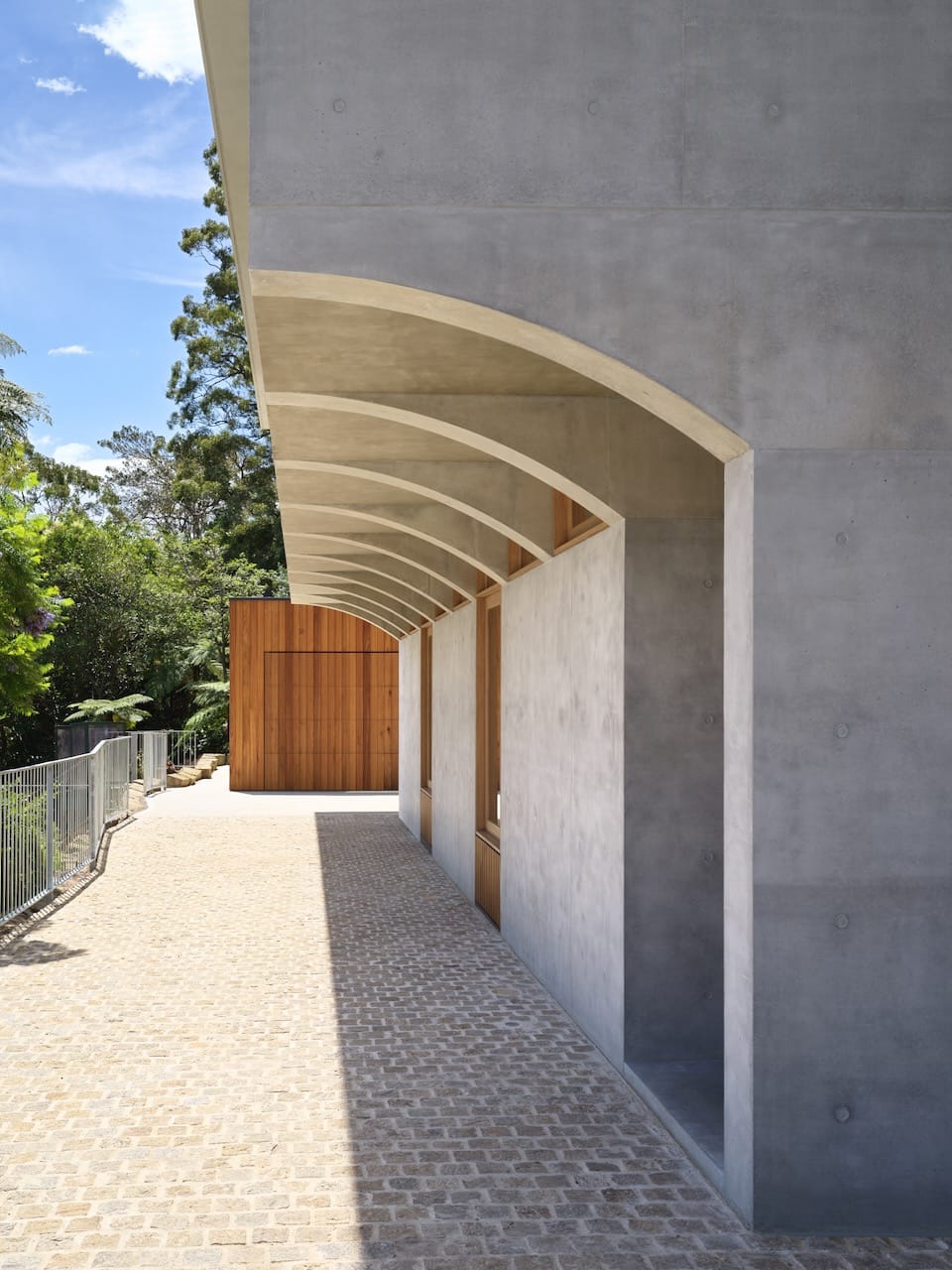Corbel House by Nick Bell Architects. Photography by Justin Alexander. Corbel-style house with concrete lower floor, with cobblestone paving and timber feature wall in background. 