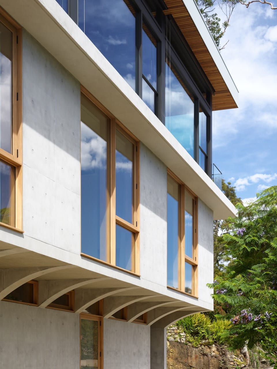 Corbel House by Nick Bell Architects. Photography by Justin Alexander. Facade of home with concrete exterior and timber windows on upper floor overhanging lower floor.