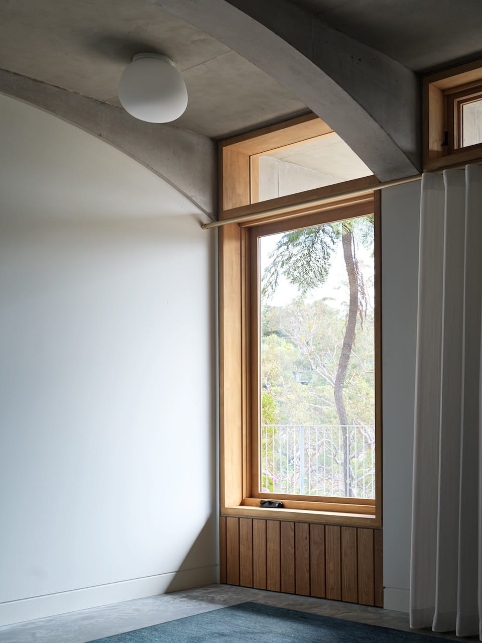 Corbel House by Nick Bell Architects. Photography by Justin Alexander. Timber window frame with paneled bottom portion, and gold curtain rail with white sheers. 