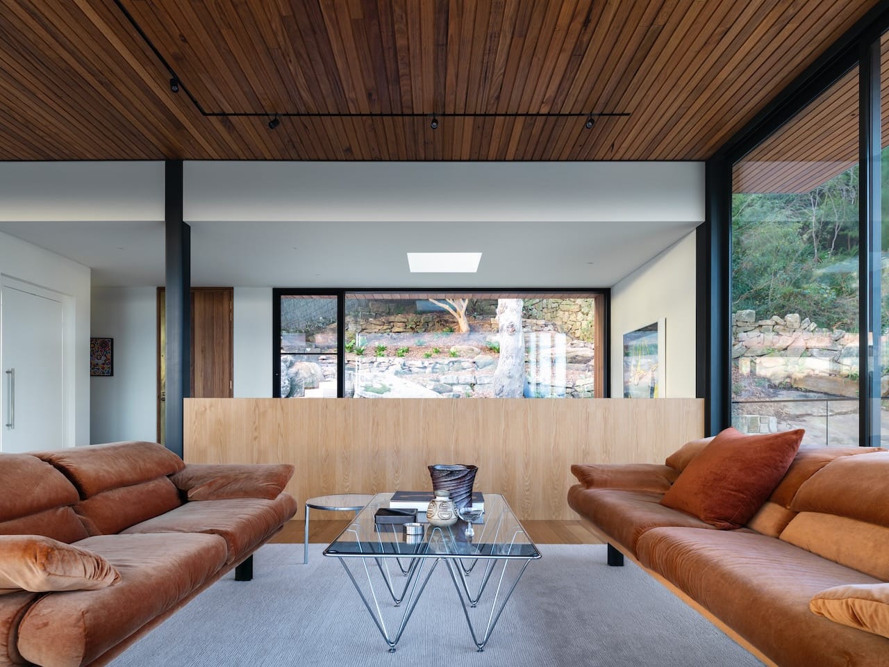 Corbel House by Nick Bell Architects. Photography by Justin Alexander. Living space with two brown corduroy couches, glass coffee table and timber dividing wall in background. 