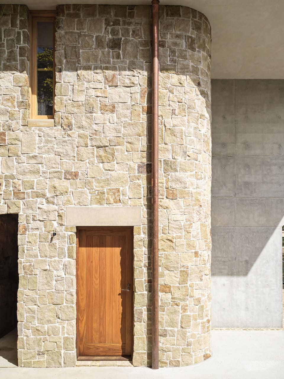 Corbel House by Nick Bell Architects. Photography by Justin Alexander. Facade of home with sandstone exterior, timber door and exposed copper plumbing. 