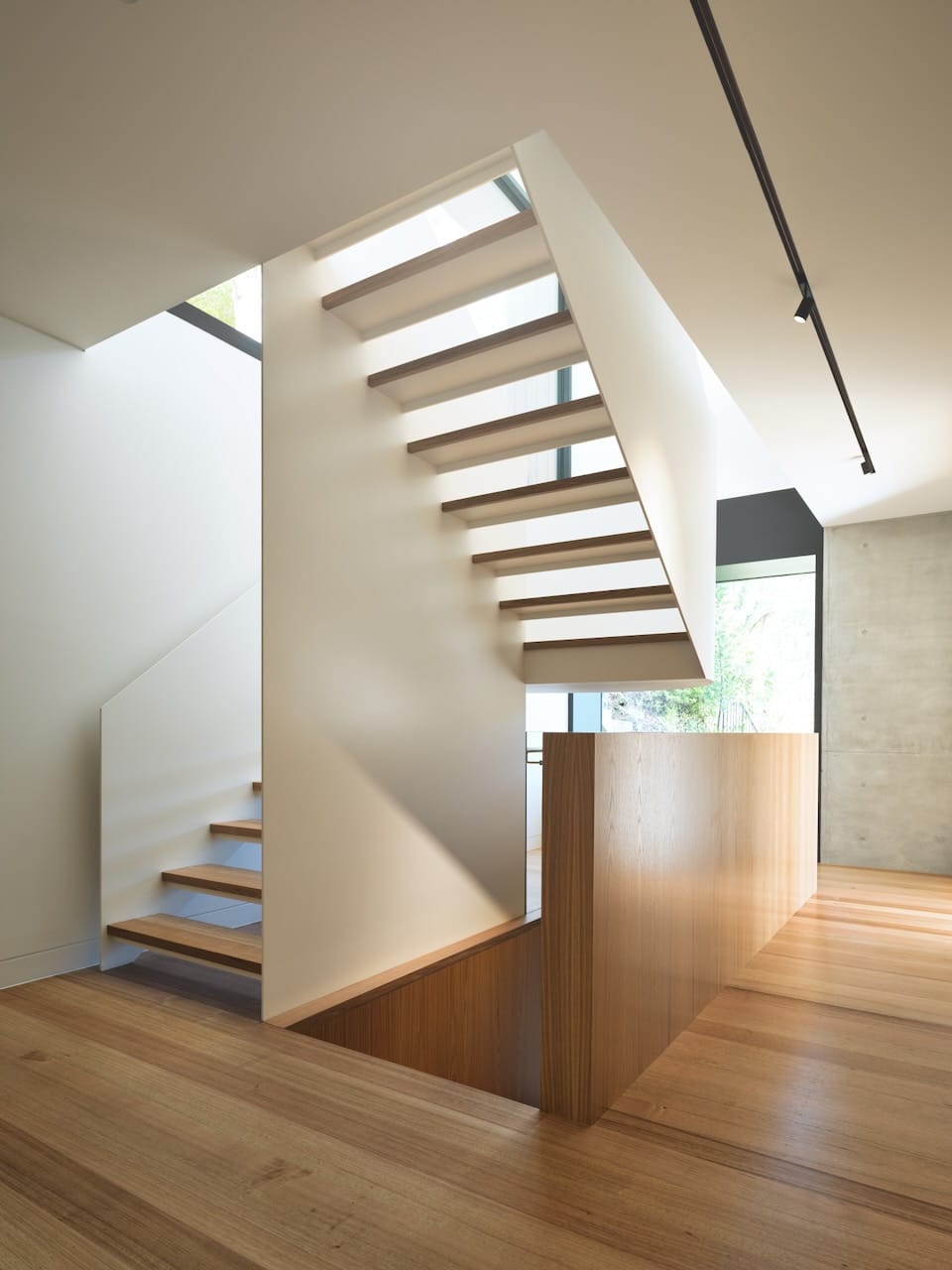 Corbel House by Nick Bell Architects. Photography by Justin Alexander. Staircase with white balustrades and timber steps, in room with concrete walls and timber floorboards. 