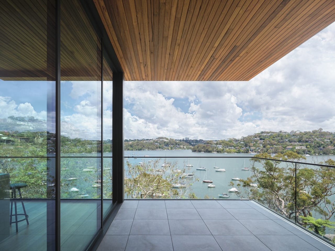 Corbel House by Nick Bell Architects. Photography by Justin Alexander. Concrete tiled balcony with glass balustrade overlooking harbour and hillside. 