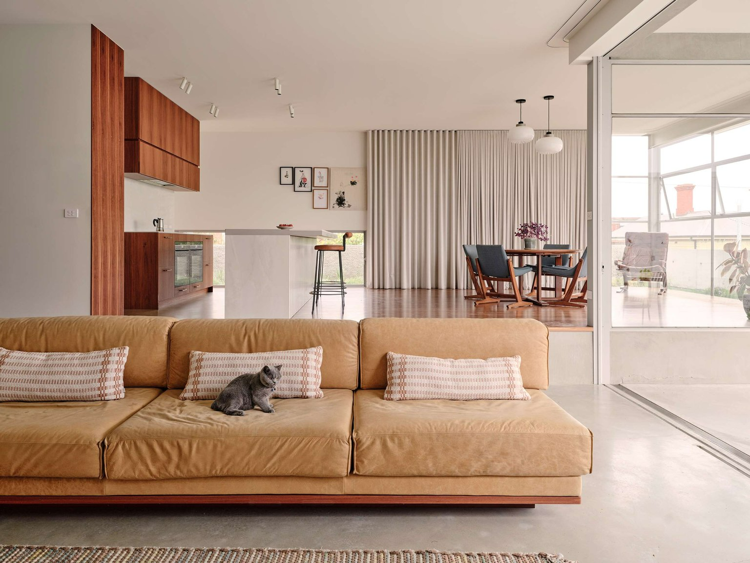 Salmon House by True Story. Photography by Dean Bradley. Open plan living, dining and kitchen with timber and polished concrete floors, a tan suede couch and timber cabinetry. 