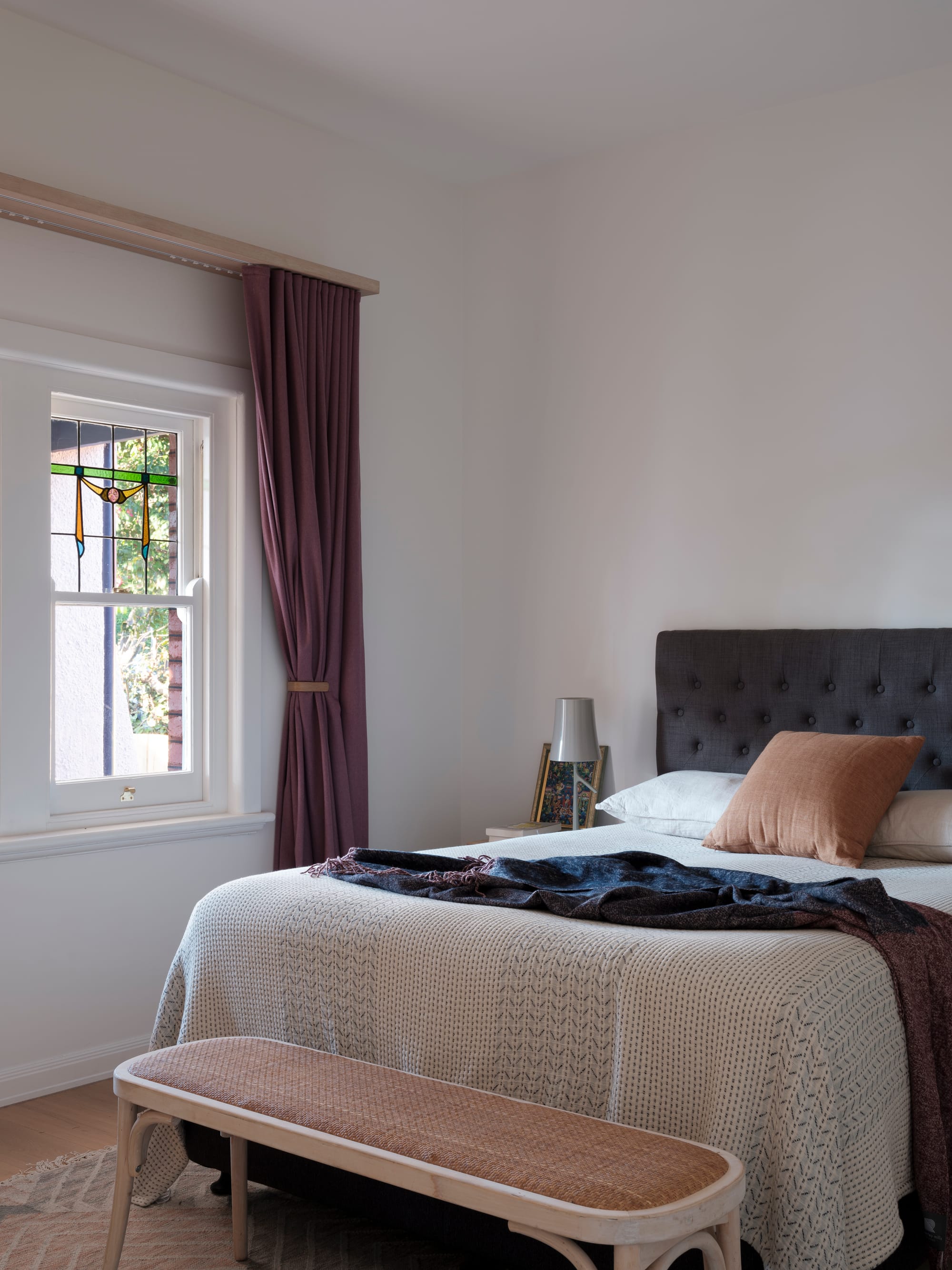 Merrilands by BIJL Architecture. Photography by Tom Ferguson. Bedroom with plum curtains, white walls, timber footstall at end of bed and graphite-coloured bedhead.