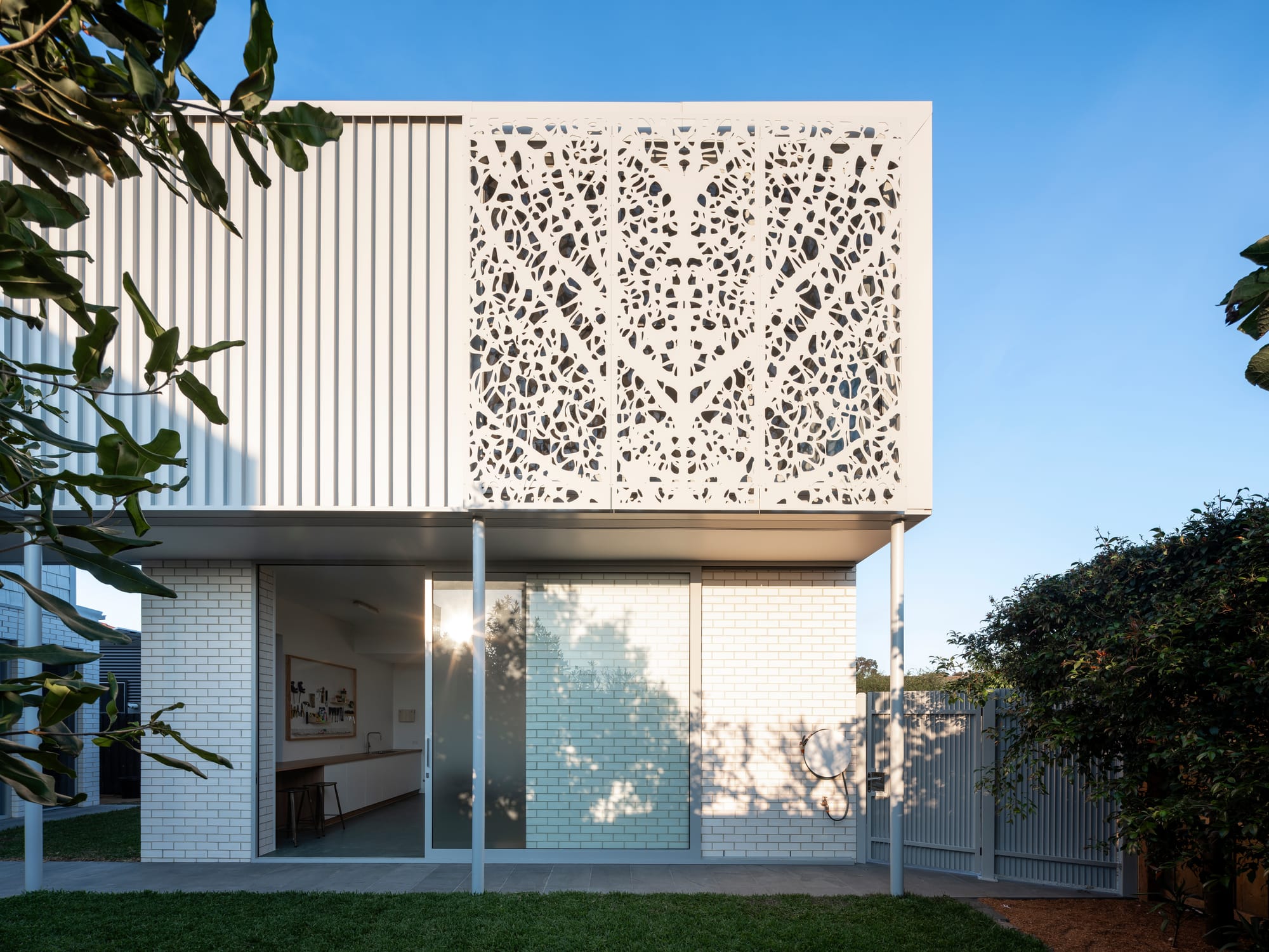 Merrilands by BIJL Architecture. Photography by Tom Ferguson. Exterior of home with decorative screening with cut outs, white brick ground floor and metal clad exterior. 