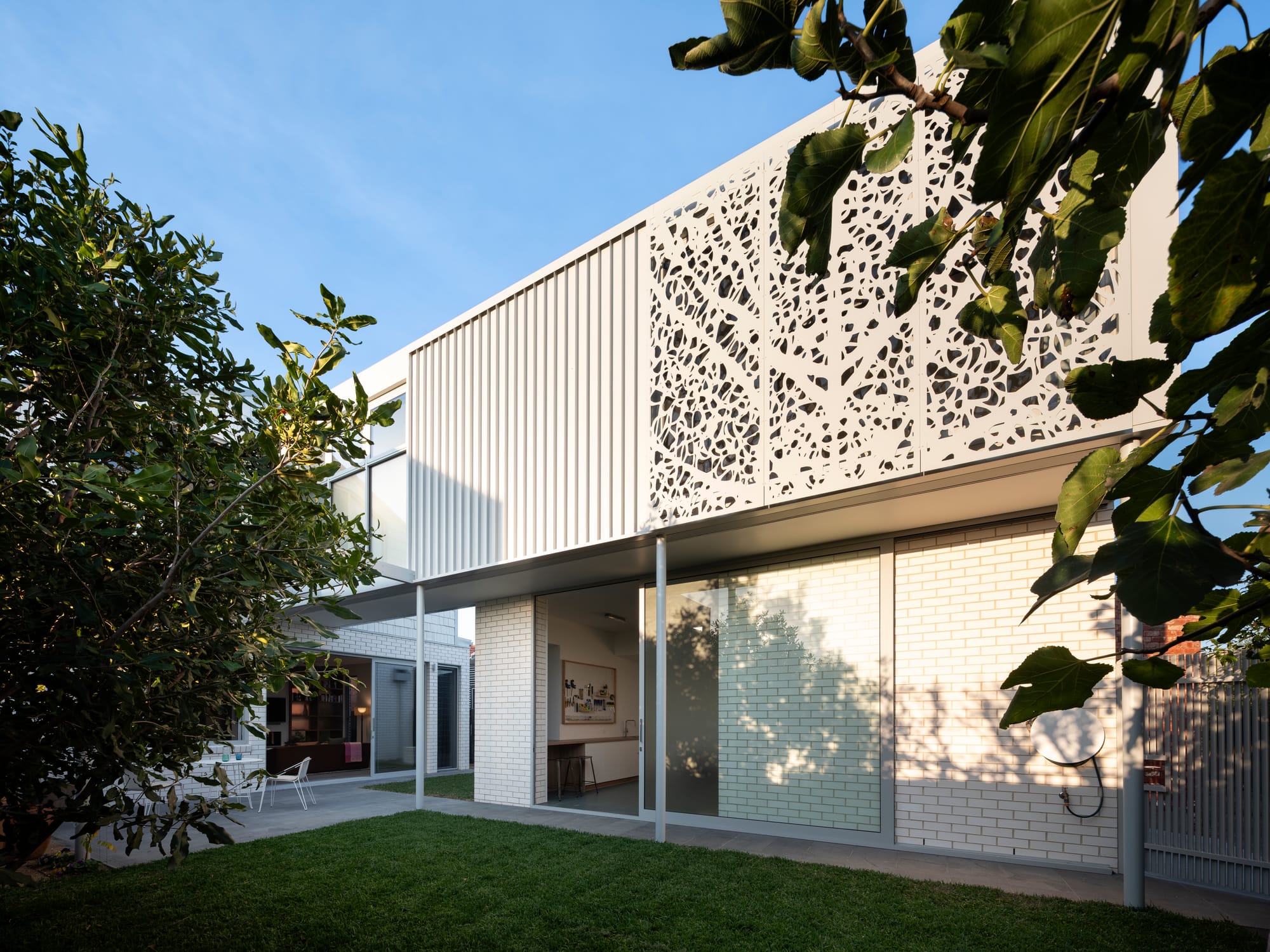 Merrilands by BIJL Architecture. Photography by Tom Ferguson. Exterior of home with white brick finish on ground floor, clad and decorative screening on top floor and green grass backyard. 