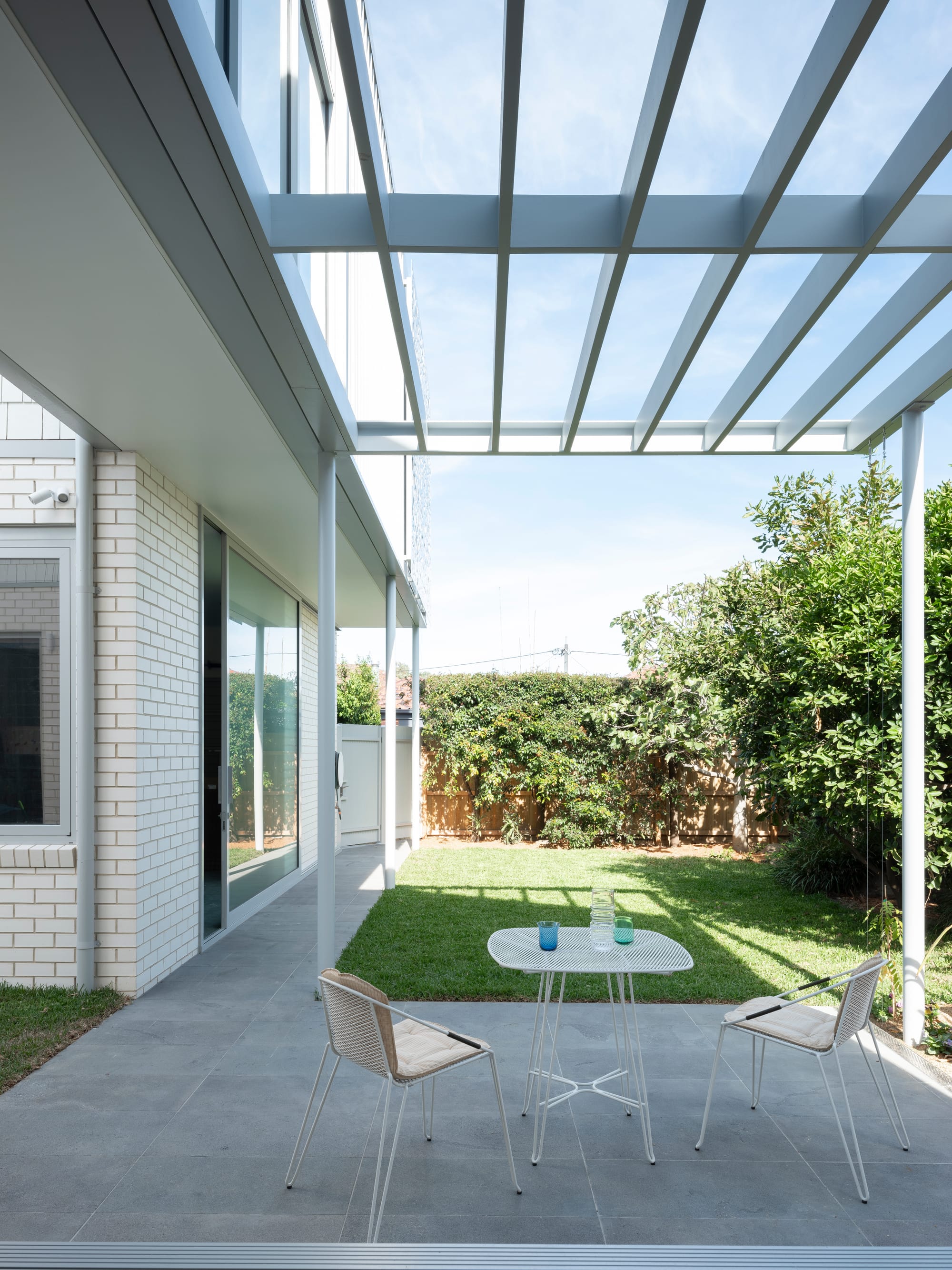 Merrilands by BIJL Architecture. Photography by Tom Ferguson. Outdoor patio with concrete pavers and simple white outdoor furniture looking over grassed backyard. 
