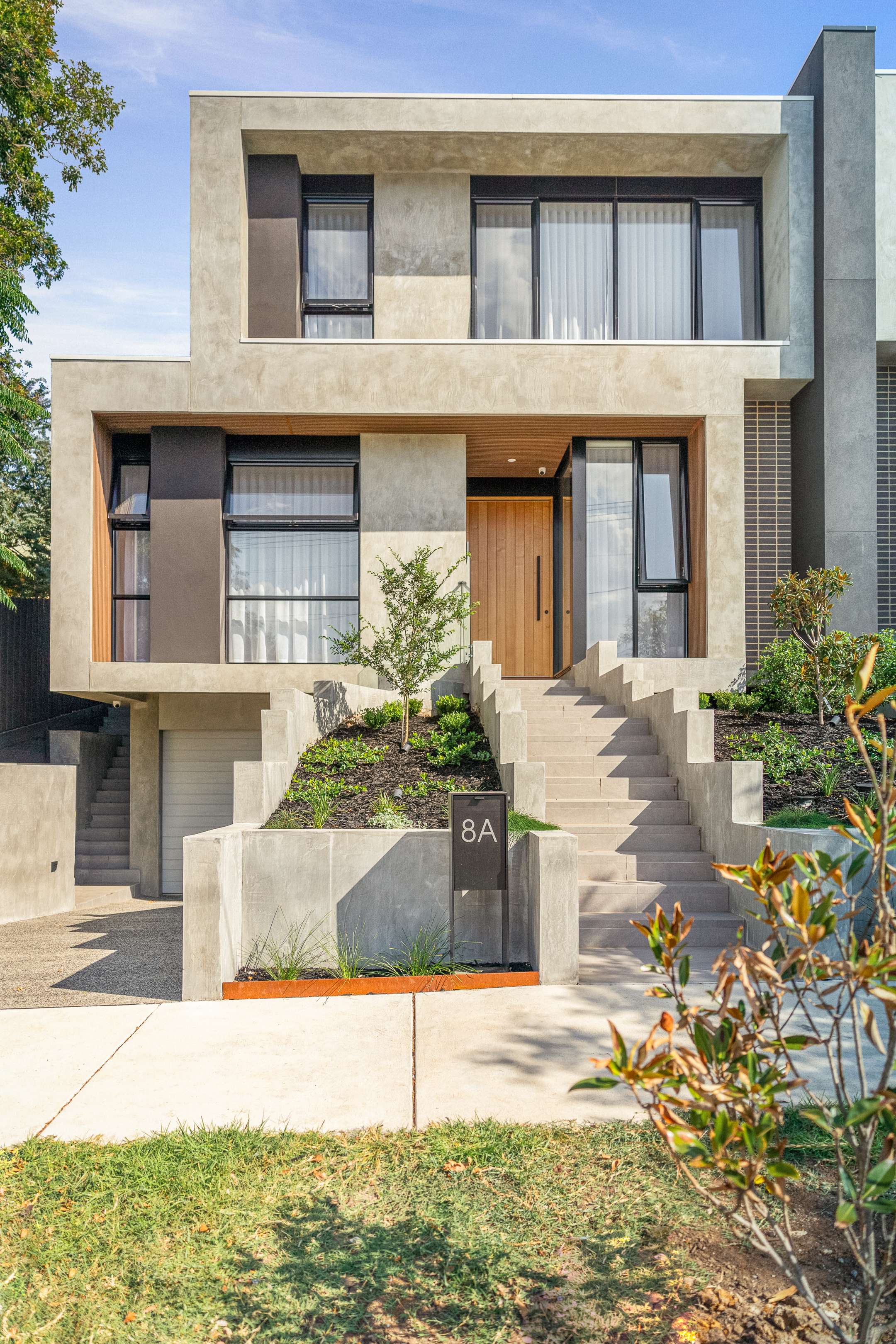 Essendon by Prem.Built. Image copyright of Prem.Built. Multi-storey contemporary residential home with concrete exterior, steps and garden beds, and timber door and window frames.