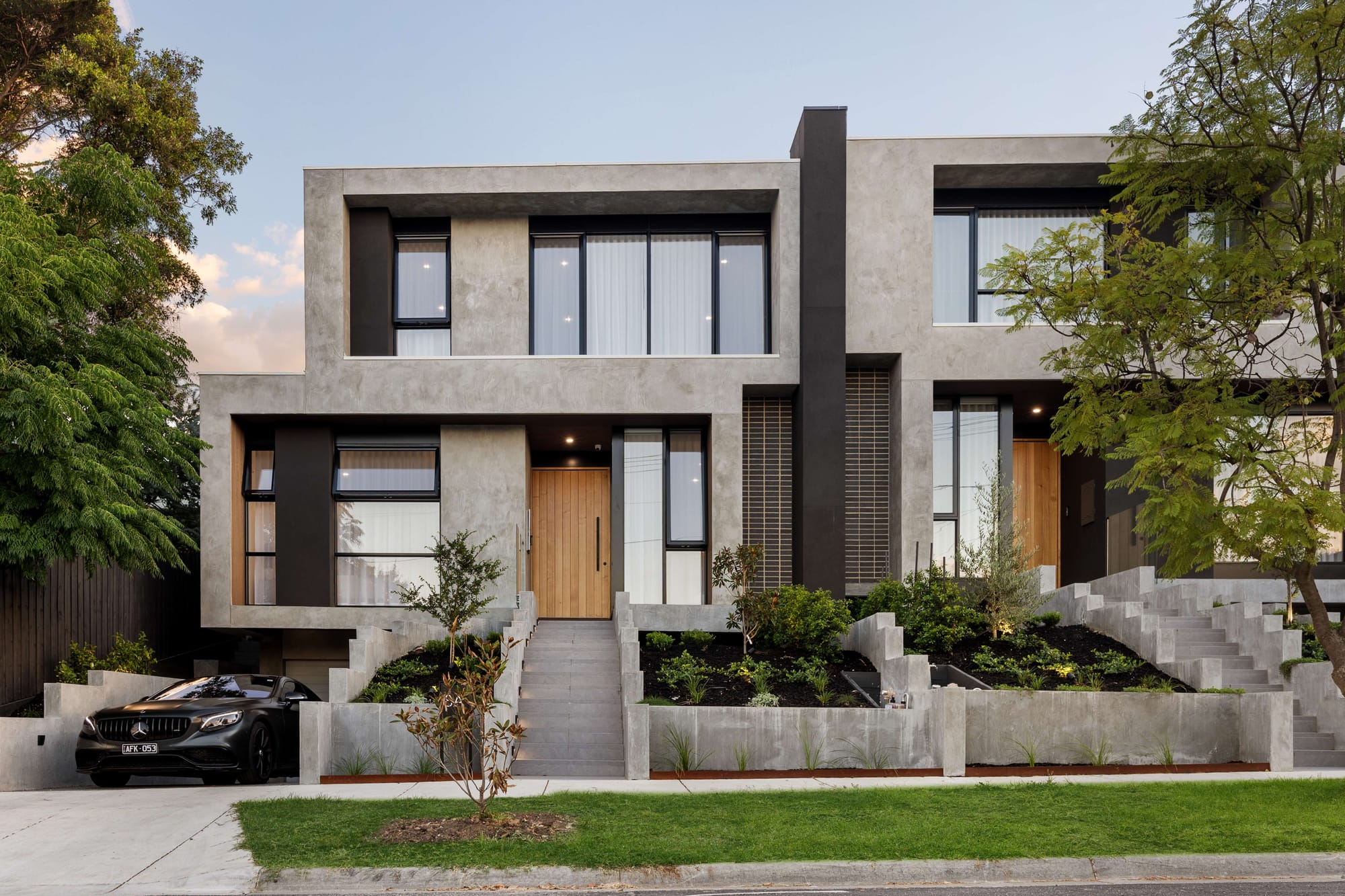 Dany and Mark Chalhoub of Prem.Built. Two men in beige outfits smiling, one sitting on couch and one standing behind. 