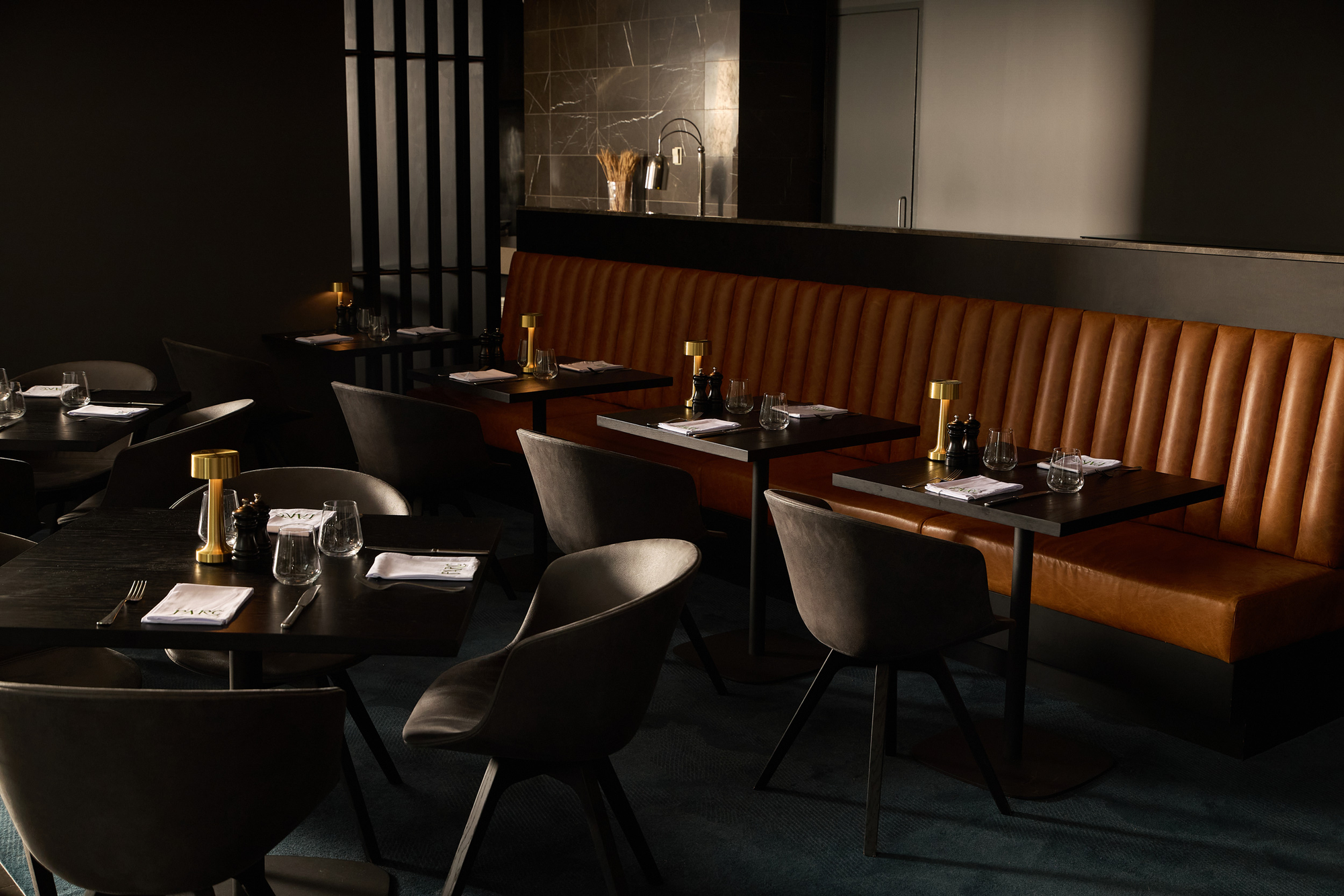 PARC Brasserie & Bar by PACT Architects. Photographer unknown. Interior of bar with brown leather booth seating, black leather sets and navy carpets. 
