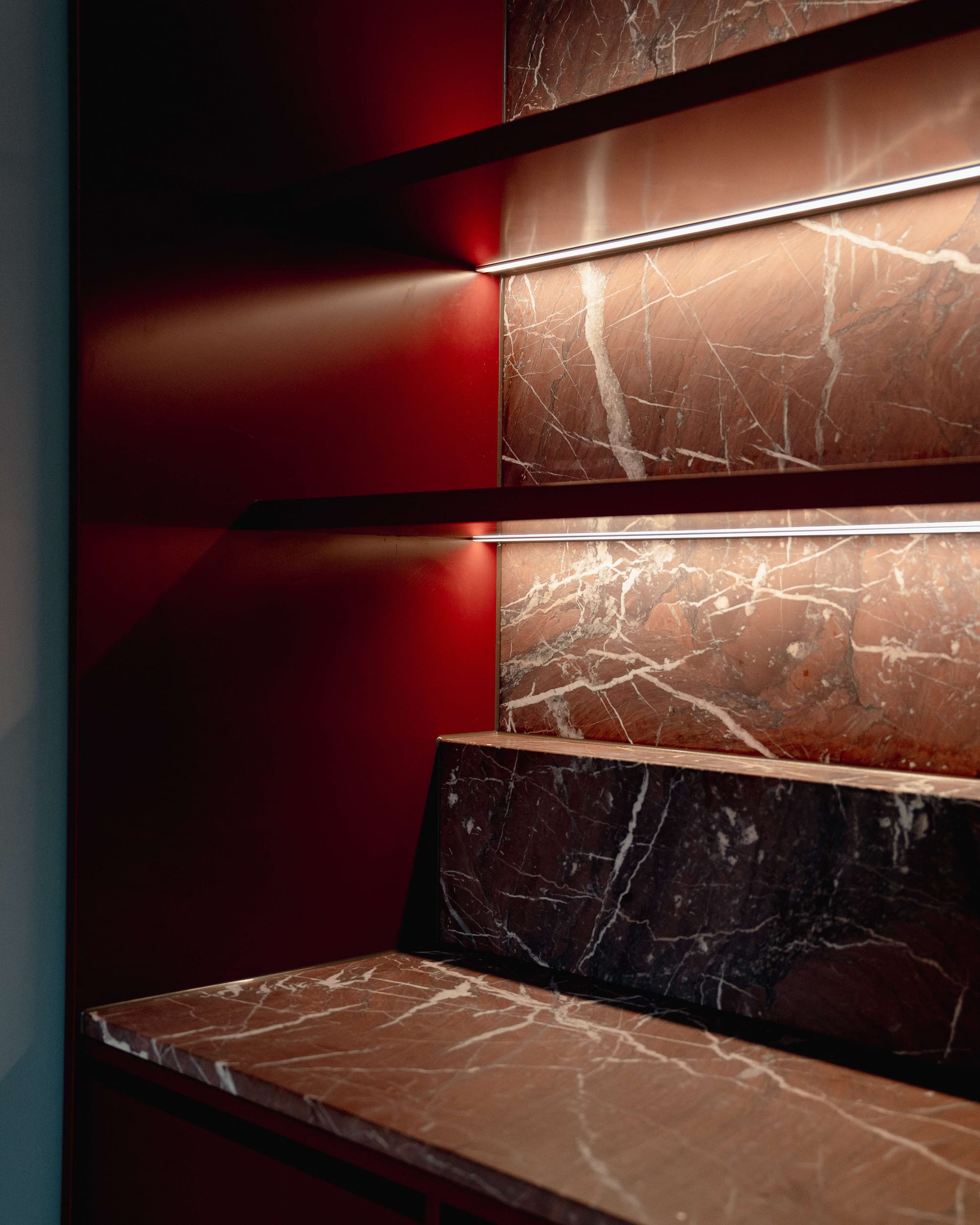 Murrumbeena by PREM.BUILT. Image copyright of Prem.Built. Integrated storage unit with dark burgundy stone countertop and splashback, burgundy and navy painted walls and under-shelf lighting. 