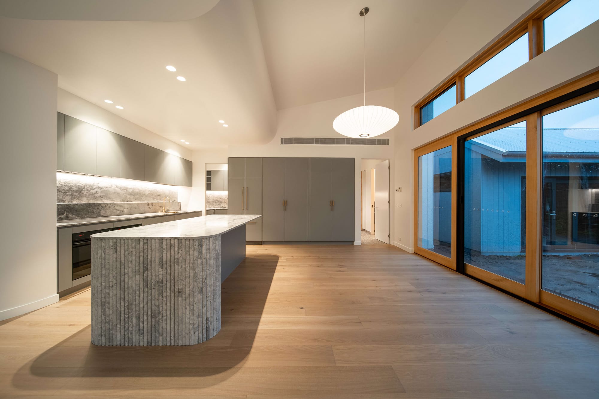 Port Melbourne 2.0 by PREM.BUILT. Image copyright of Prem.Built. Open plan kitchen space with stone island bench, timber floors and sliding timber and glass doors. 