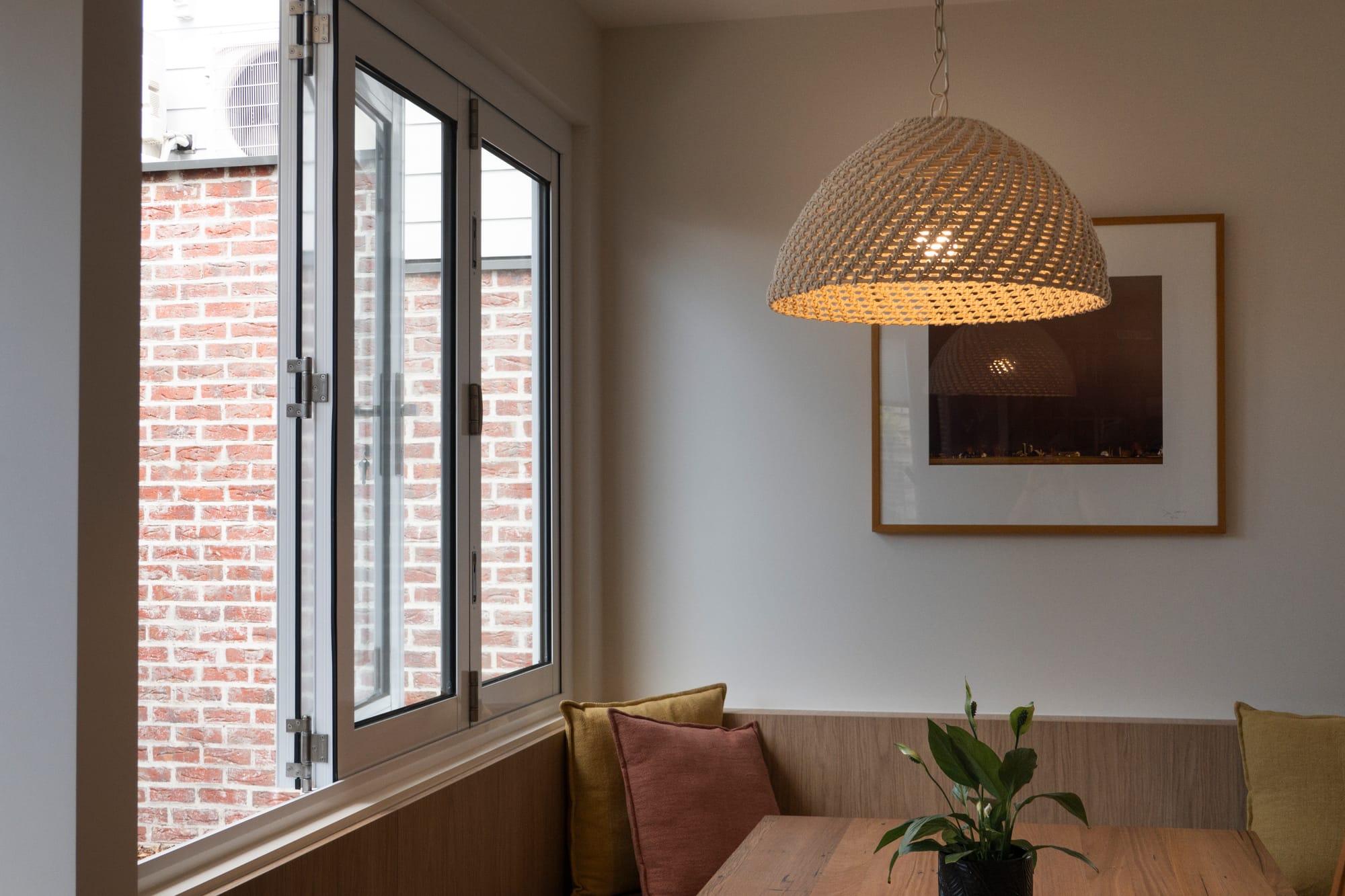Port Melbourne 2.0 by PREM.BUILT. Image copyright of Prem.Built. Breakfast nook with timber bench seating and table, mustard and terracotta cushions, rattan pendant light and white windows.