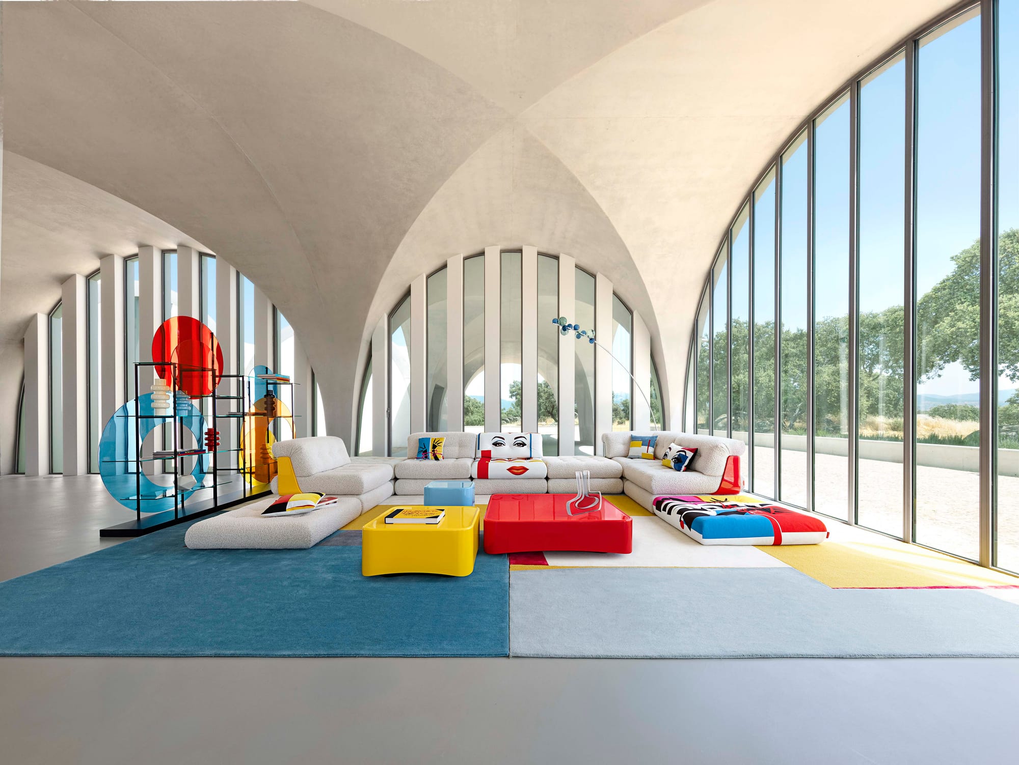 The Lounge Collection by Roche Bobois. Image copyright of Roche Bobois. White modular couch with patterned pillows and sections, with red and yellow coffee tables. 