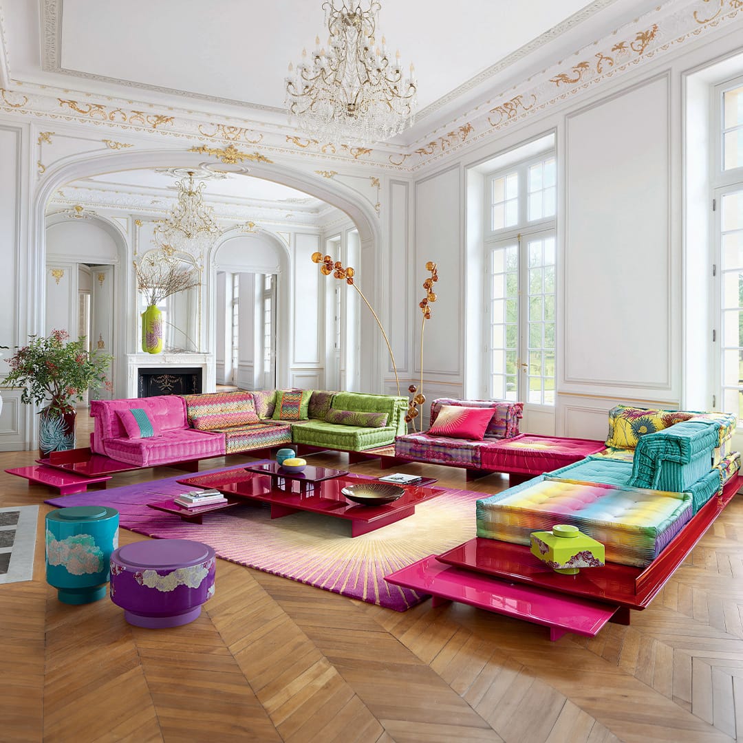 Mah Jong by Roche Bobois. Image copyright of Roche Bobois. Hot pink gloss platform with multicoloured and patterned modular couch cushions, in room with herringbone floors and ornate ceilings. 