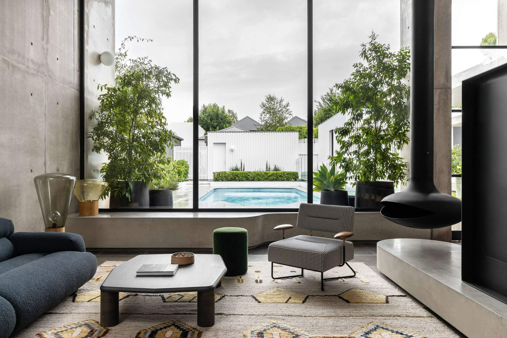 Rose Park House by Studio Gram. Photography by Timothy Kaye. Interior living space with concrete bench window seating lining space, with floating black fireplace and views out over pool. 