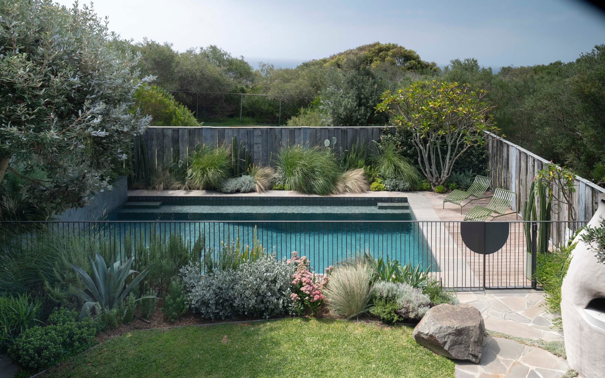 Stone House by Secret Gardens. Elevated view of the pool garden surrounded by layered coastal planting and weathered timber fencing.