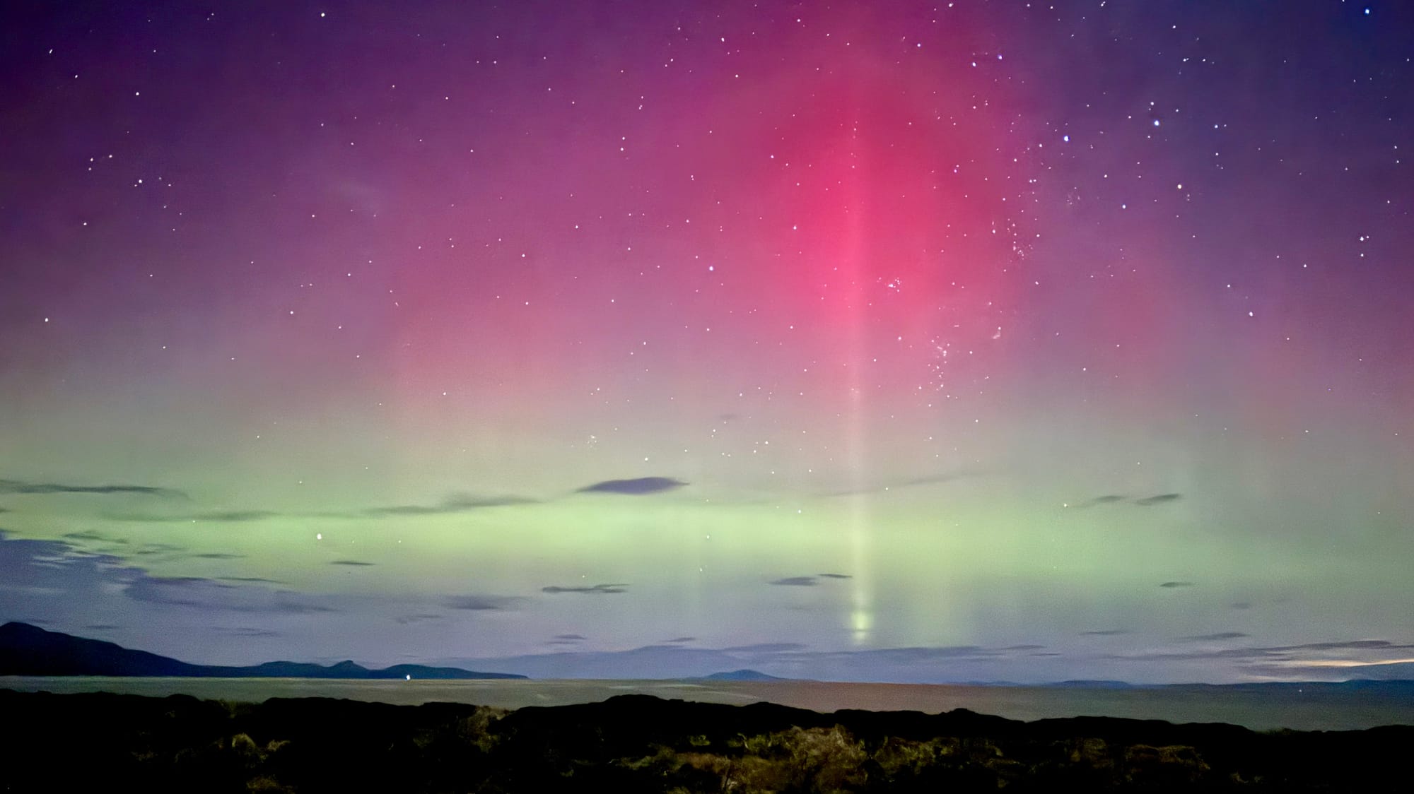 Aurora Australia at Studio Tasmania. Photography by Studio Tasmania. Aurora with pink and teal tones over ocean and hilly landscape in background. 