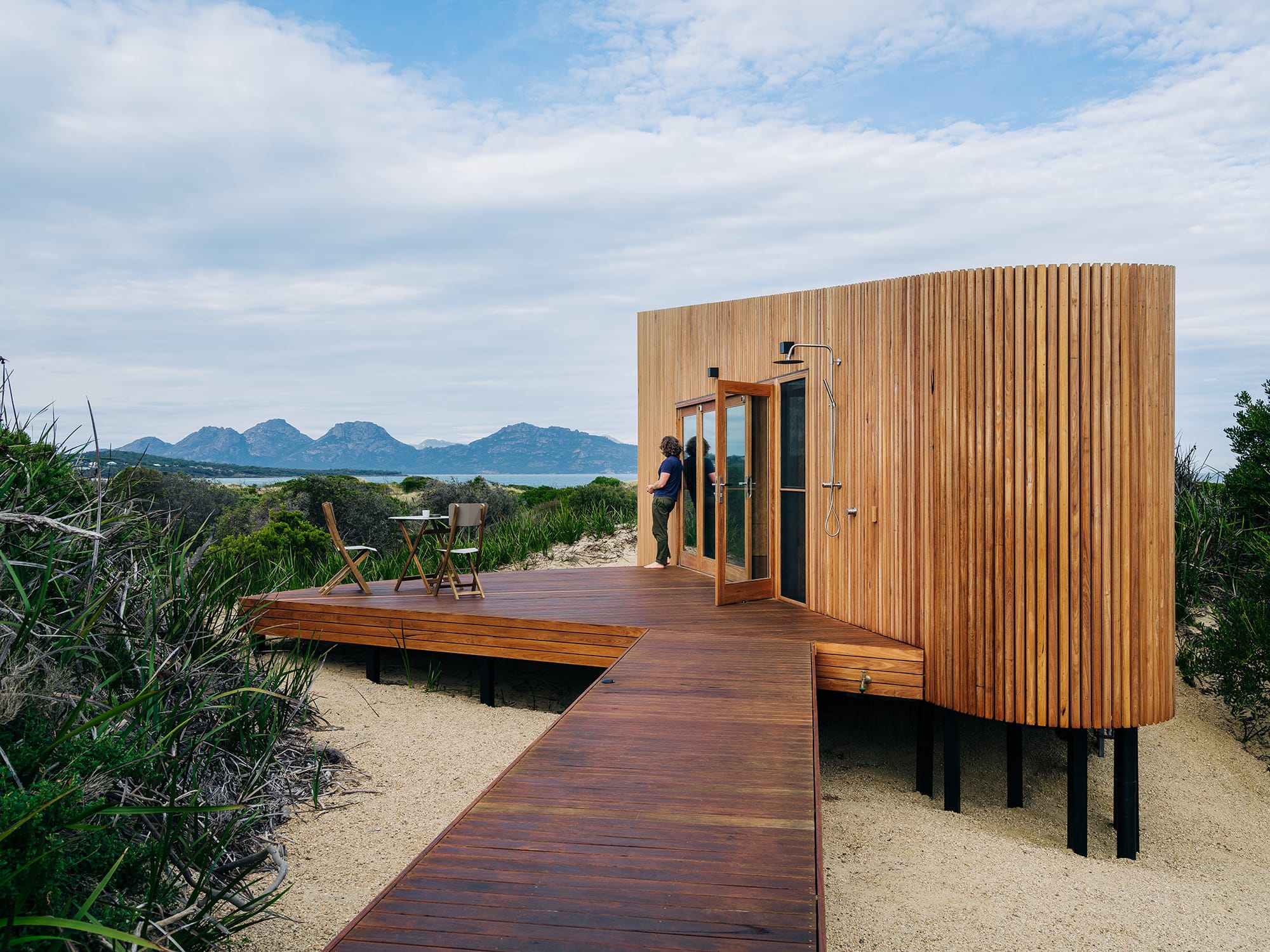 Studio Tasmania. Photography by Adam Gibson. Boardwalk over sand leading to timber clad beach pod. 