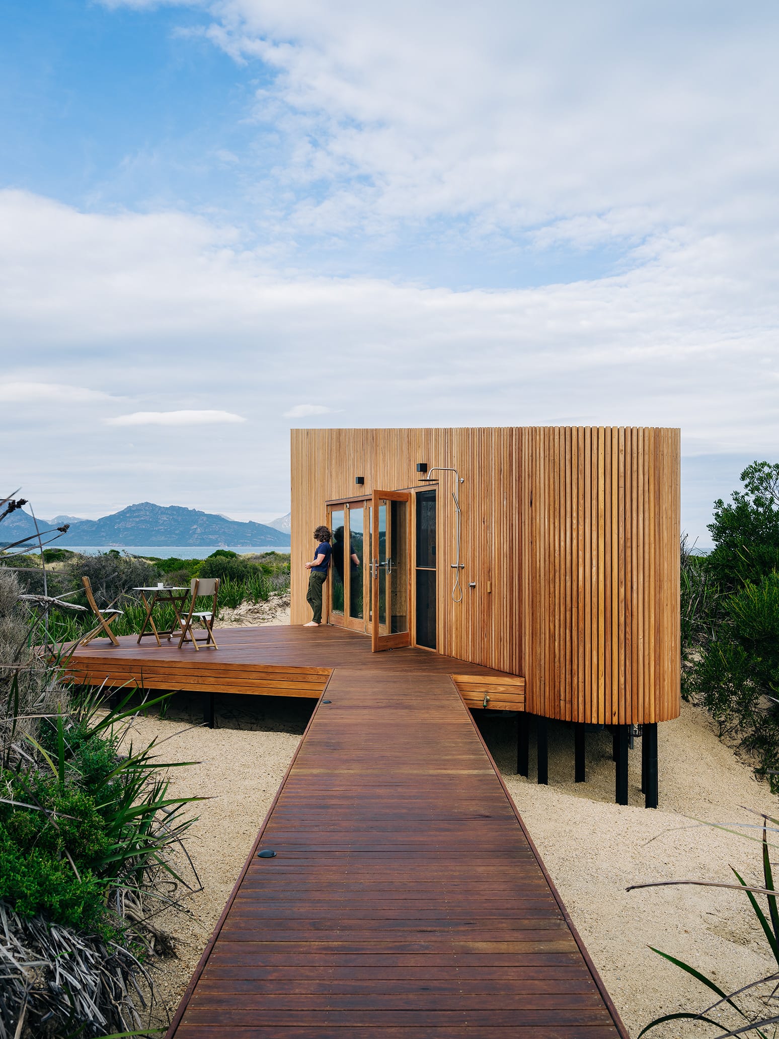 Studio Tasmania. Photography by Adam Gibson.  Boardwalk over sand leading to timber clad beach pod with timber deck. 
