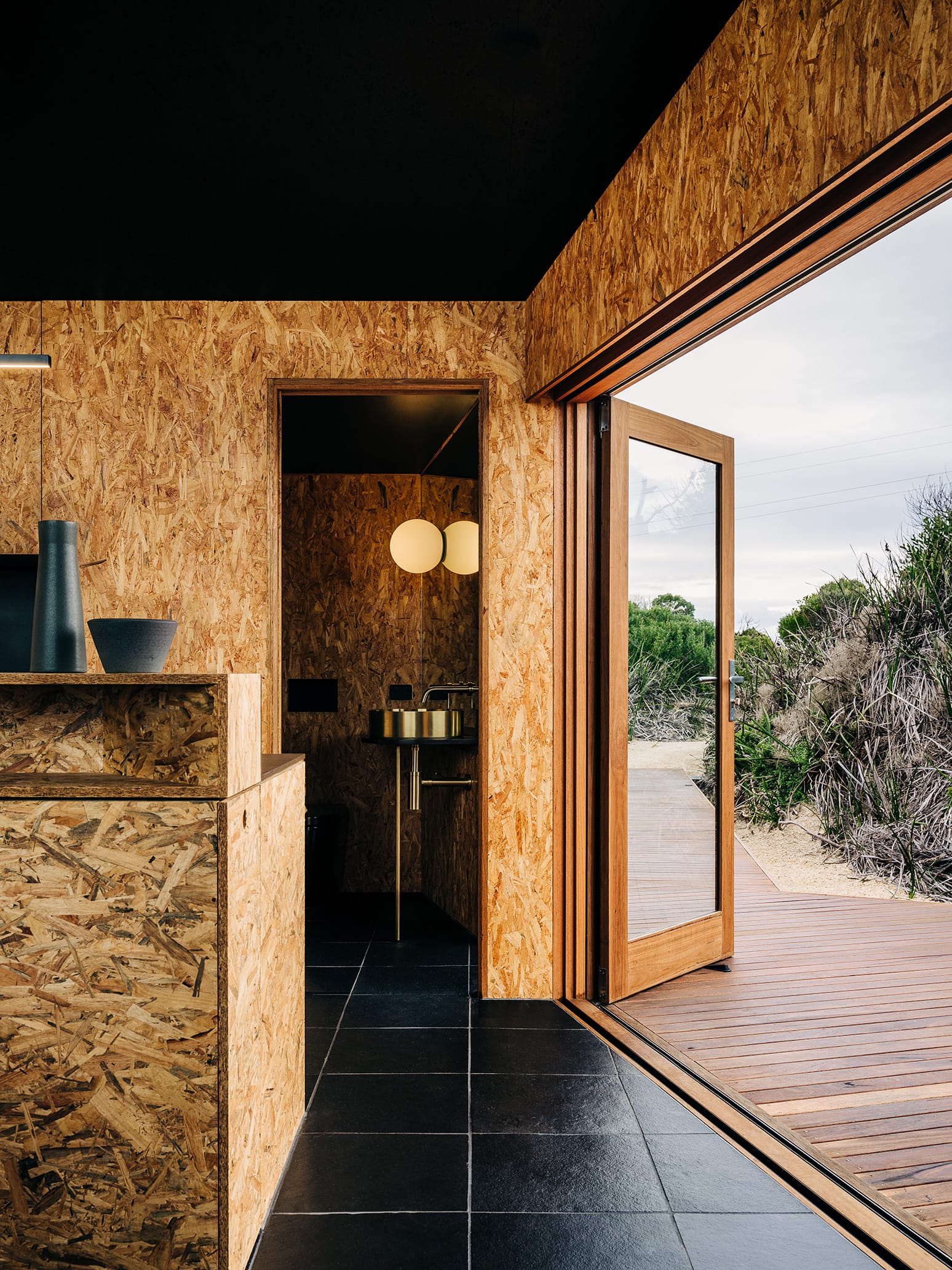 Studio Tasmania. Photography by Adam Gibson. Timber and glass doors opening black tiled interior onto outdoor timber deck.