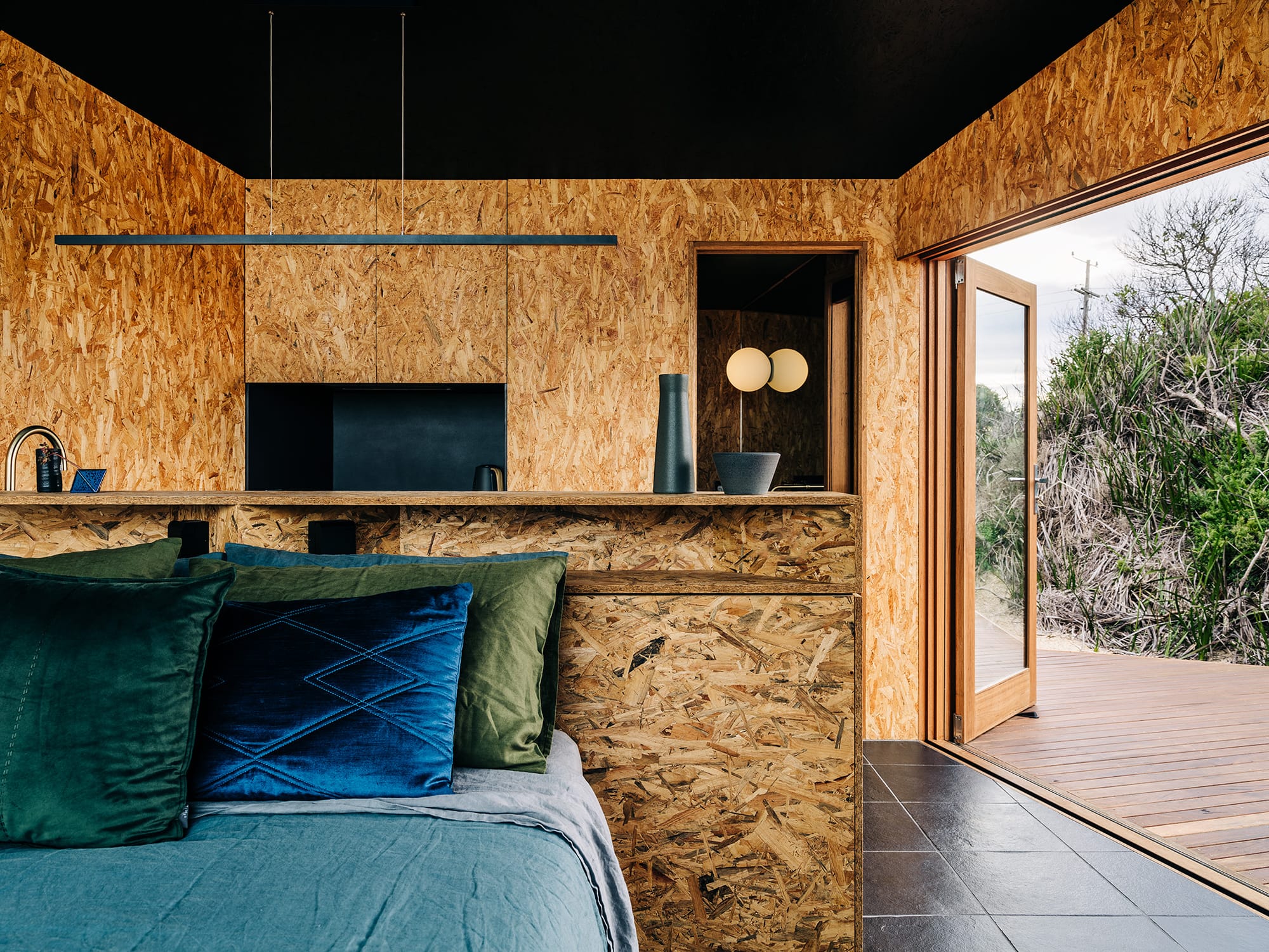 Studio Tasmania. Photography by Adam Gibson. Studio space with timber walls. counters and doors, and bed with jewel-toned bedding. 