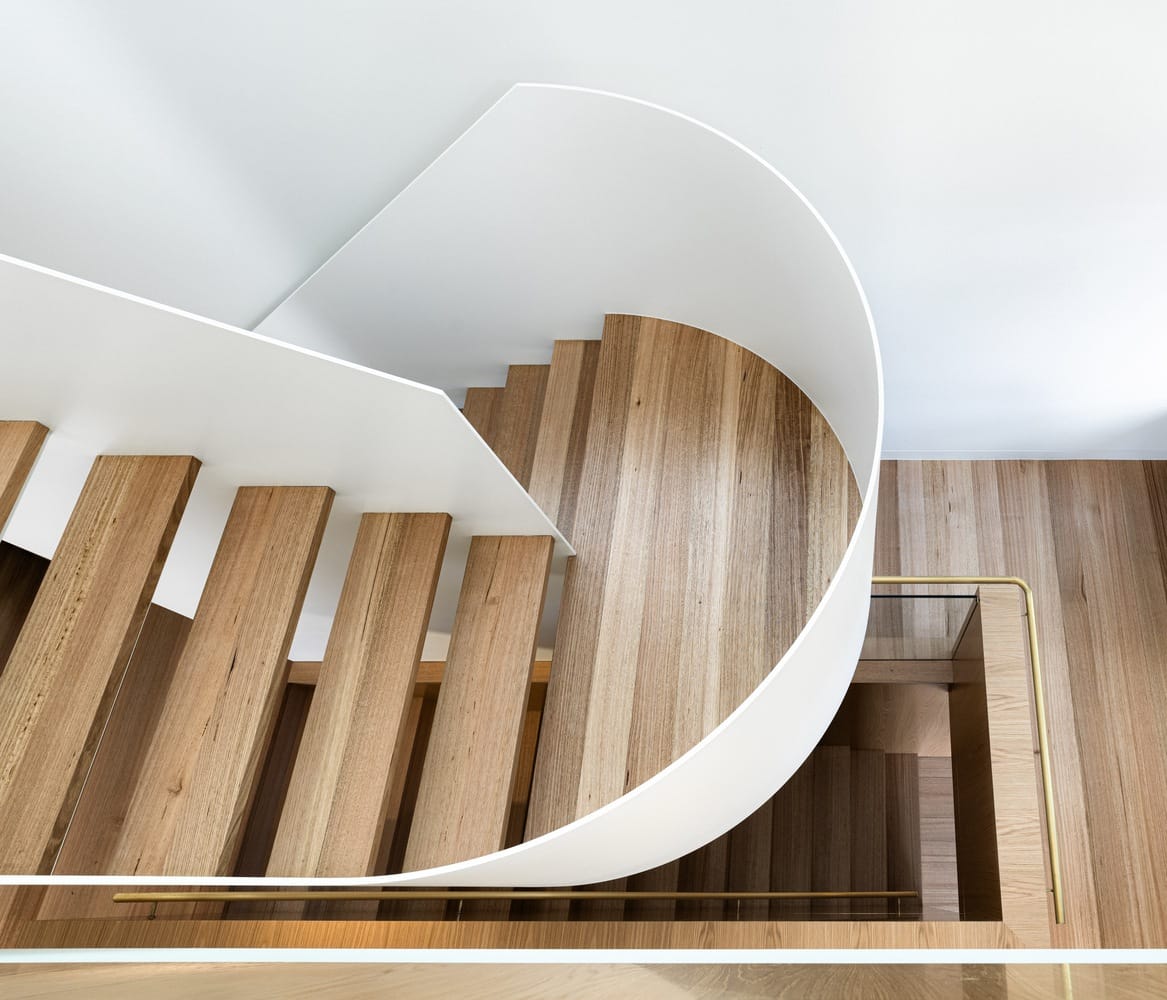 Corbel House by Nick Bell Architects. Photography by Justin Alexander. Aerial view of curved staircase, with timber steps and flooring, white steel balustrade and gold handrail. 