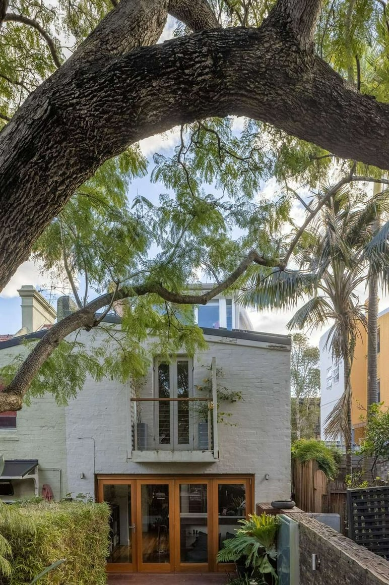 The Jacaranda Terrace, Paddington by Nathalie Scipioni Architects. Photography by Sarah Vita. Rear facade of white brick home with timber folding doors onto brick patio. 