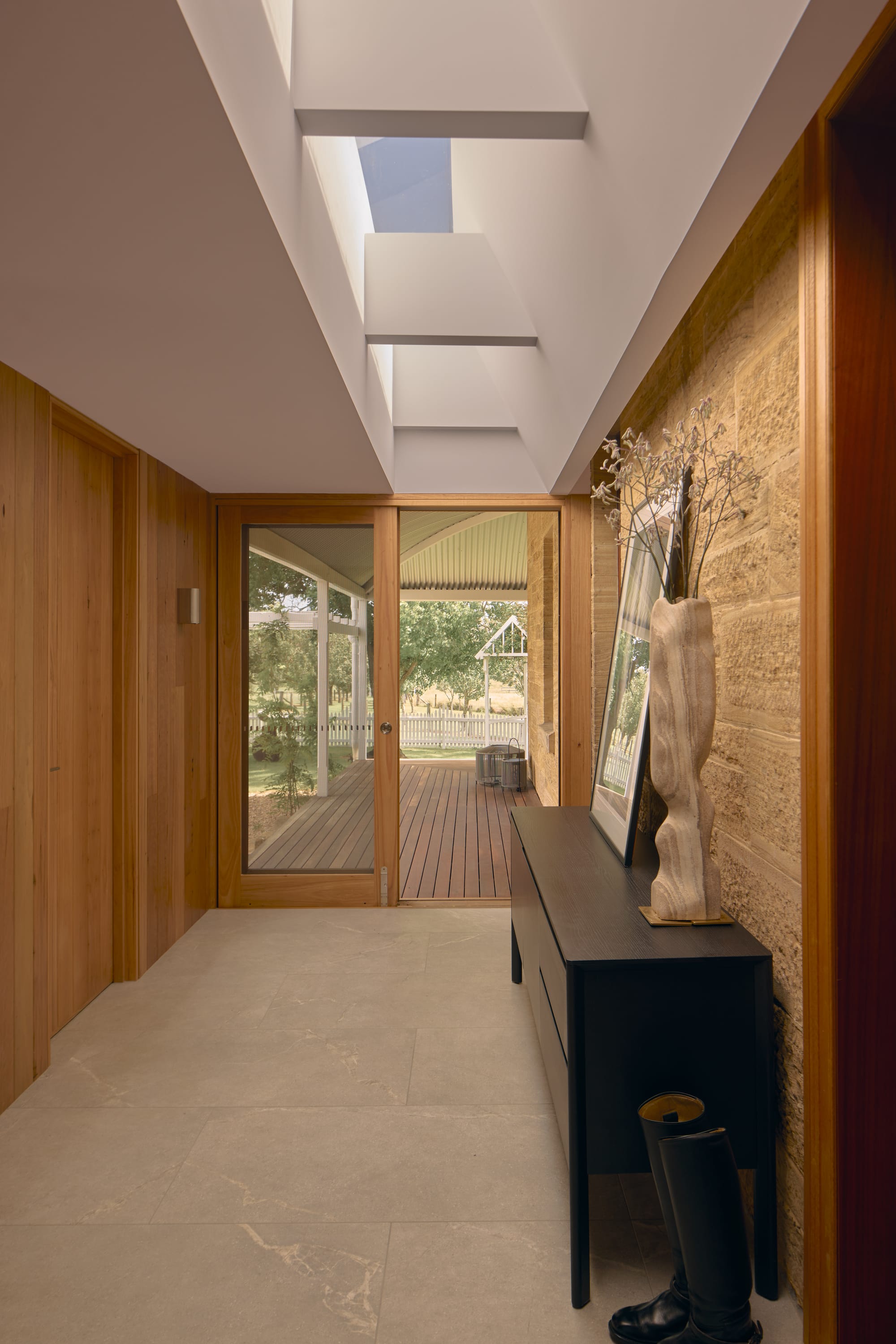 Binnum Homestead by Alexandra Buchanan Architecture. Photography by Cieran Murphy. Hallway with stone paved floors, timber walls, timber doorframe leading to timber deck, and white ceiling with skylights. 